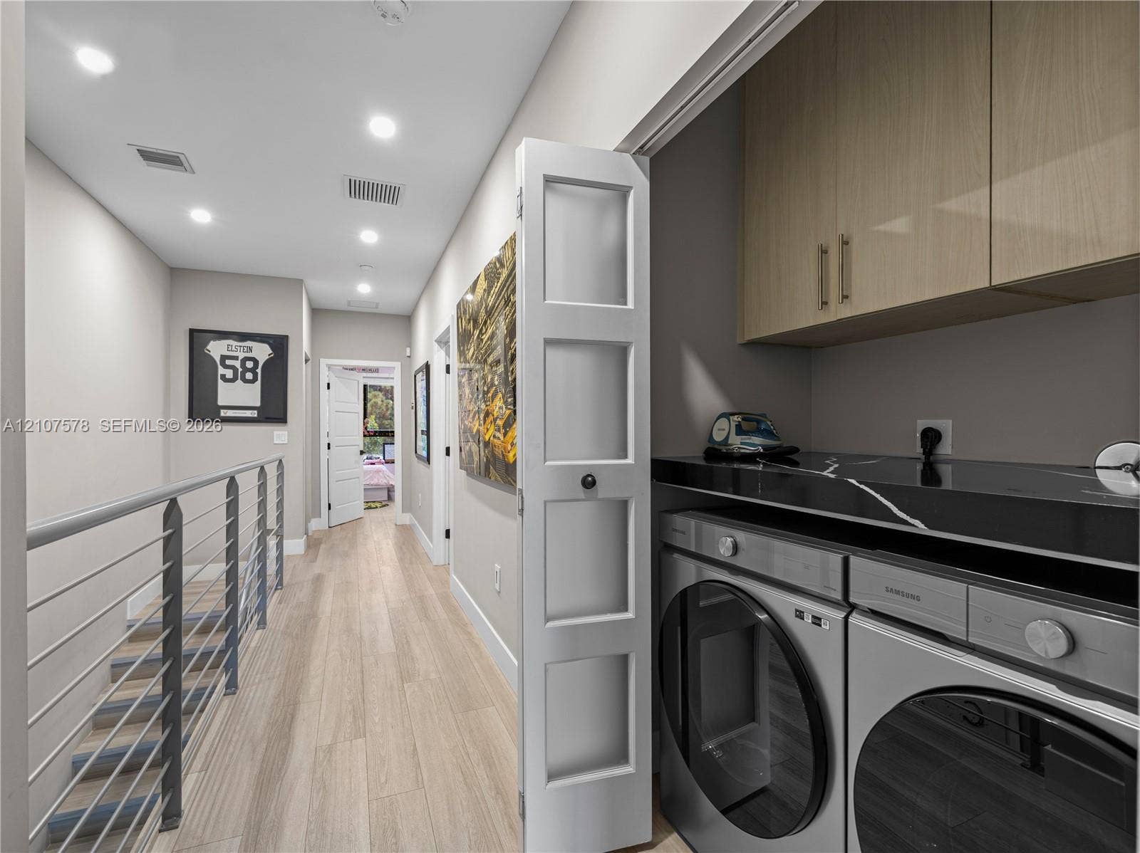 307 SW 10th Street, Fort Lauderdale, FL 33315 Laundry closet featuring light-toned cabinetry, high-gloss solid surface countertop, and recessed ceiling lighting, accompanied by a hallway with wood-finish flooring and a metal cable railing system