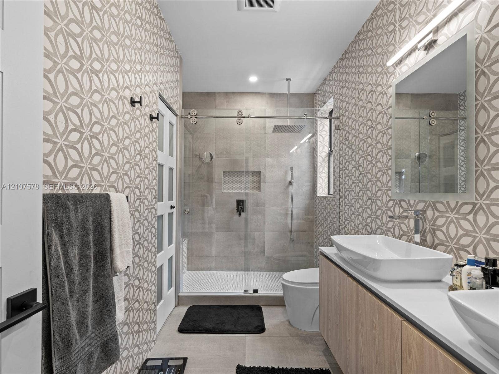 307 SW 10th Street, Fort Lauderdale, FL 33315 Floating wood-finish vanity with dual vessel sinks, walk-in shower with glass enclosure and rain-style showerhead, patterned wall tile, and built-in recessed shower niche