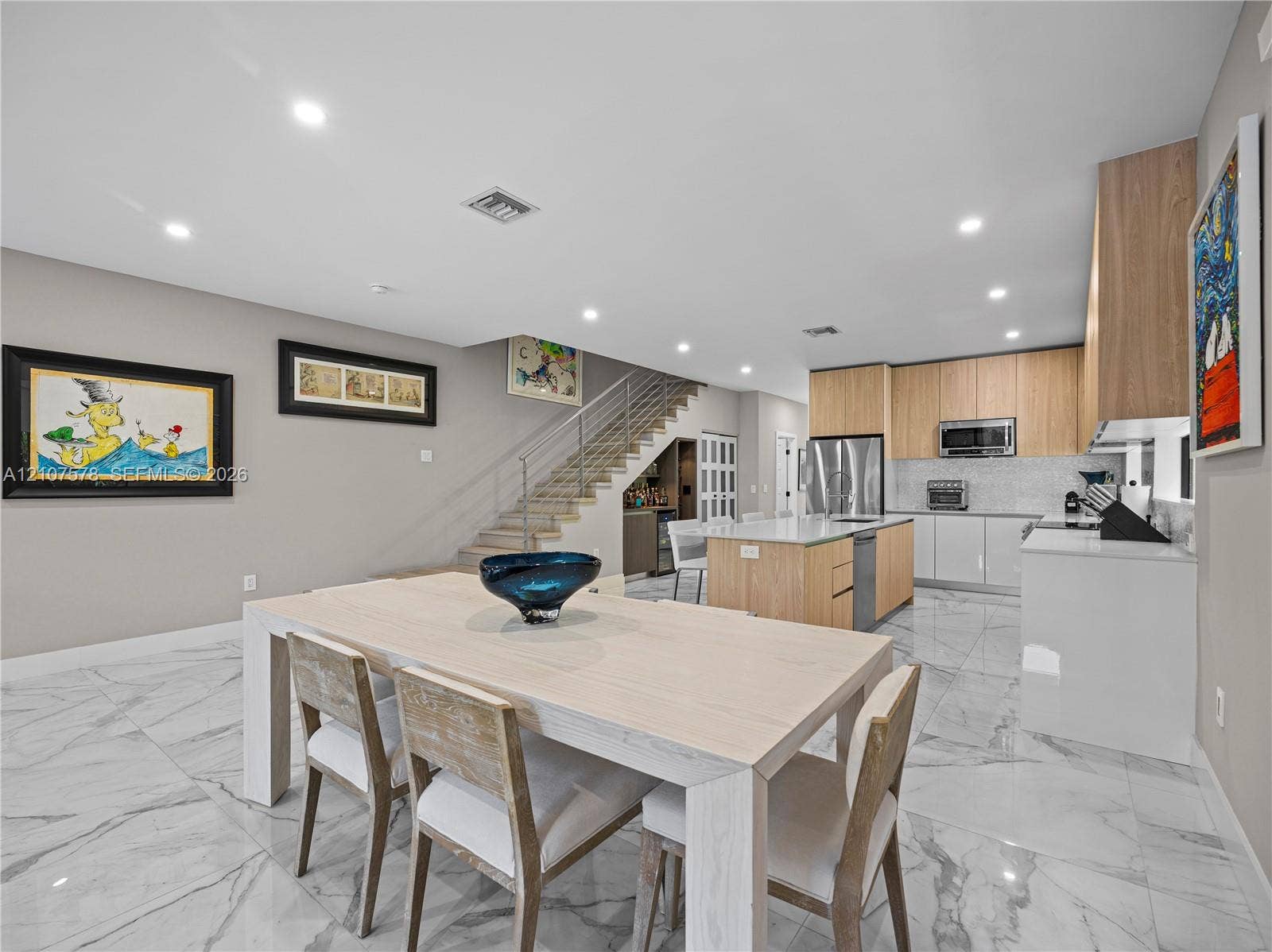 307 SW 10th Street, Fort Lauderdale, FL 33315 Modern kitchen featuring flat-panel wood cabinetry, a central island with white stone countertops, built-in stainless steel appliances, marble-patterned tile flooring, and a floating staircase with a metal railing