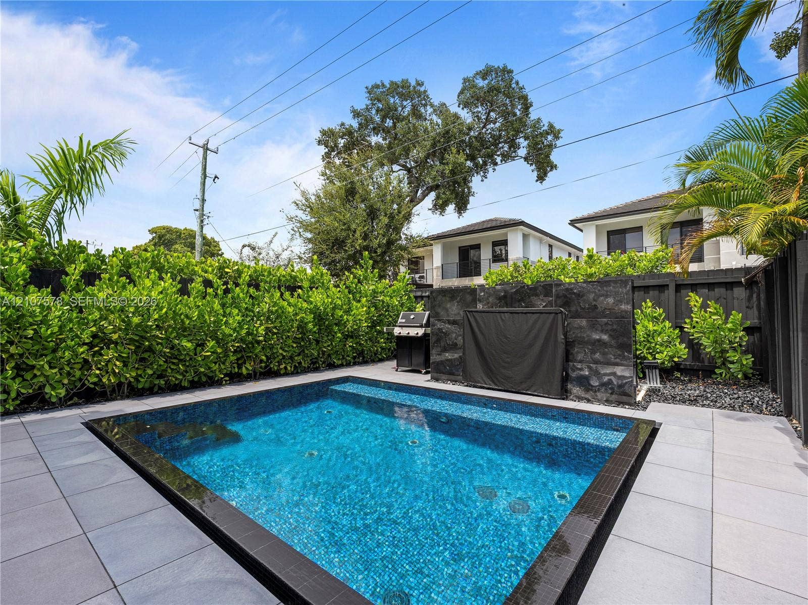 307 SW 10th Street, Fort Lauderdale, FL 33315 Private courtyard featuring a plunge pool with mosaic tile finish, large-format concrete paver decking, and a structured stone-veneer accent wall enclosed by perimeter hedging