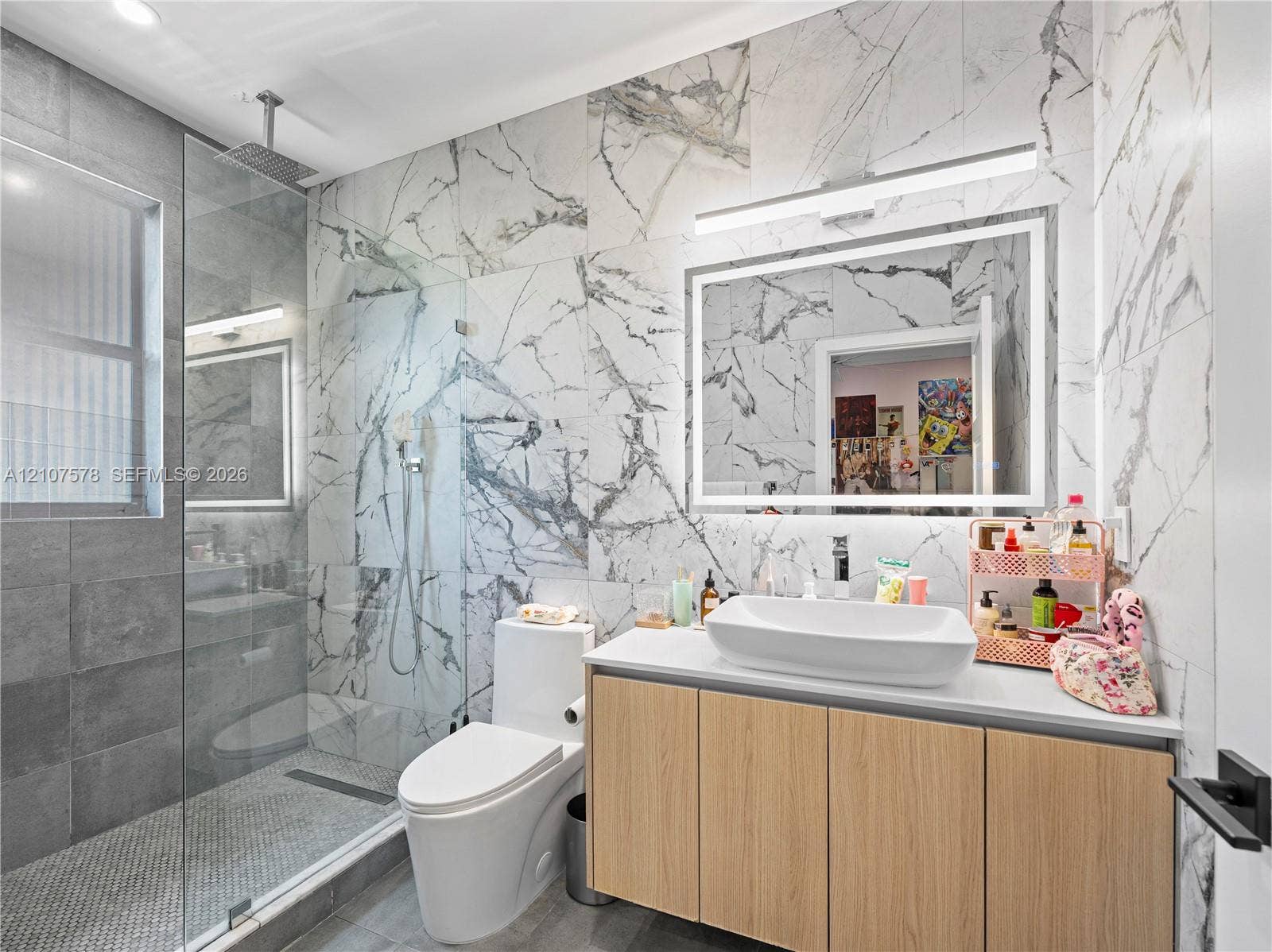 307 SW 10th Street, Fort Lauderdale, FL 33315 Bathroom featuring floor-to-ceiling large-format veined tile, walk-in shower with a glass enclosure and rainfall showerhead, floating vanity with a vessel sink, and an integrated LED-backlit mirror
