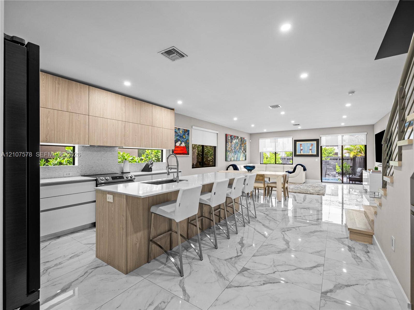 307 SW 10th Street, Fort Lauderdale, FL 33315 Kitchen featuring two-tone cabinetry with wood-finish upper cabinets, large waterfall-edge island with countertop seating, stone-finish flooring, and recessed lighting