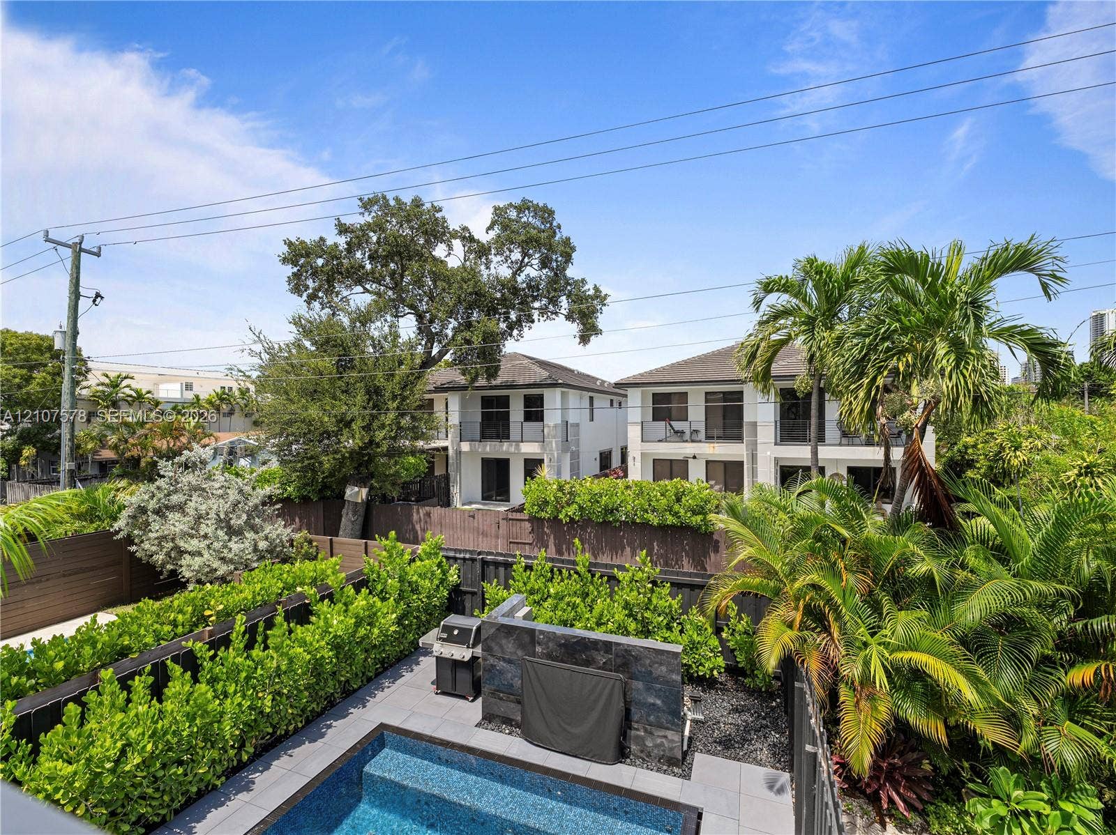 307 SW 10th Street, Fort Lauderdale, FL 33315 Backyard featuring a custom pool, tiered stone-finish accent wall, slate-style patio decking, and perimeter privacy hedges