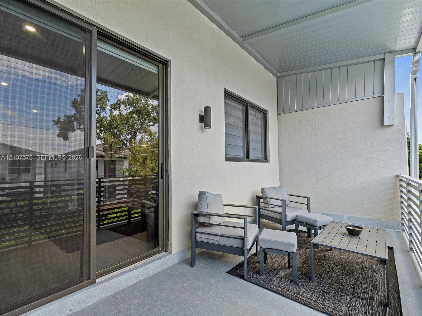 307 SW 10th Street, Fort Lauderdale, FL 33315 Covered balcony featuring sliding glass doors, horizontal slat railings, neutral stucco exterior wall, and wall-mounted exterior lighting