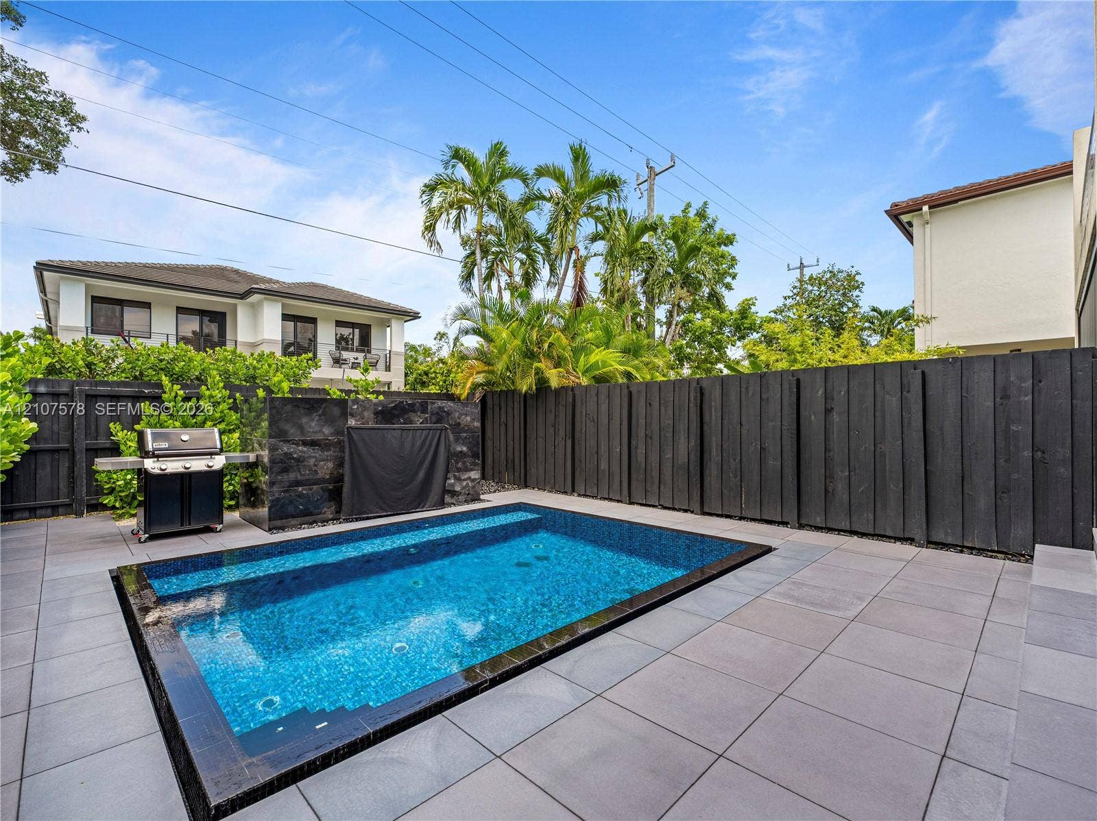 307 SW 10th Street, Fort Lauderdale, FL 33315 In-ground swimming pool with tiled surround, stone-clad water feature, and dark wood privacy fencing