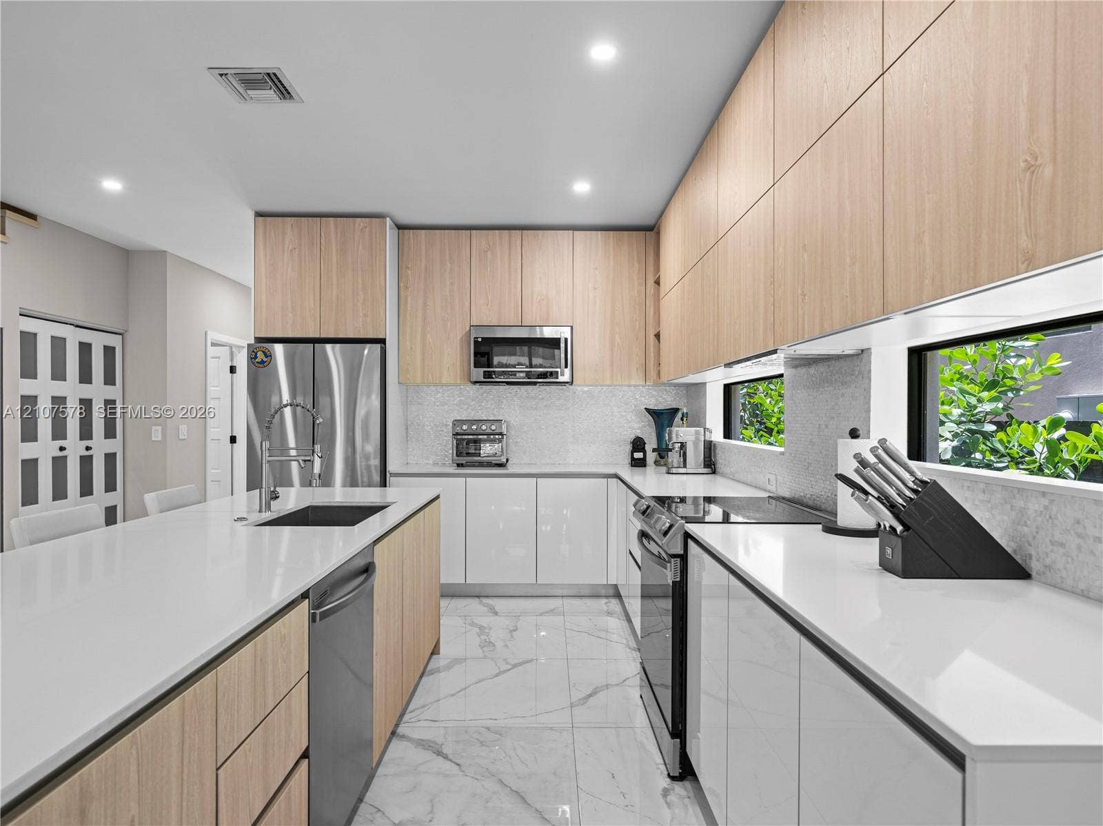 307 SW 10th Street, Fort Lauderdale, FL 33315 Kitchen featuring white quartz countertops, wood-finish flat-panel cabinetry, stainless steel appliances, marble-patterned flooring, and a horizontal backsplash window