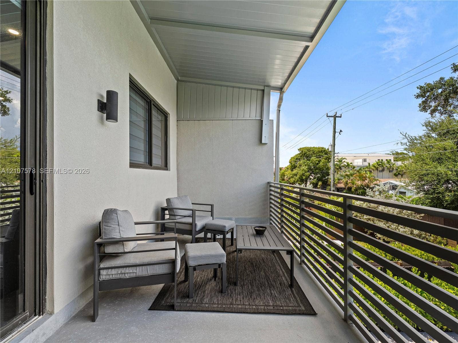 307 SW 10th Street, Fort Lauderdale, FL 33315 Covered balcony featuring a horizontal metal railing, smooth stucco exterior walls, and wall-mounted exterior cylinder lighting