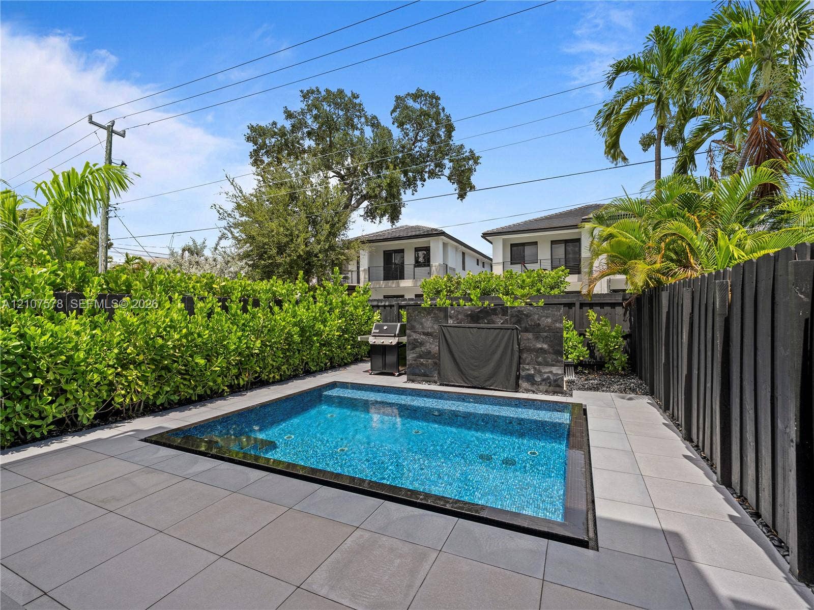 307 SW 10th Street, Fort Lauderdale, FL 33315 In-ground pool with tile surround, stone-finish accent wall, and perimeter hedge privacy screening