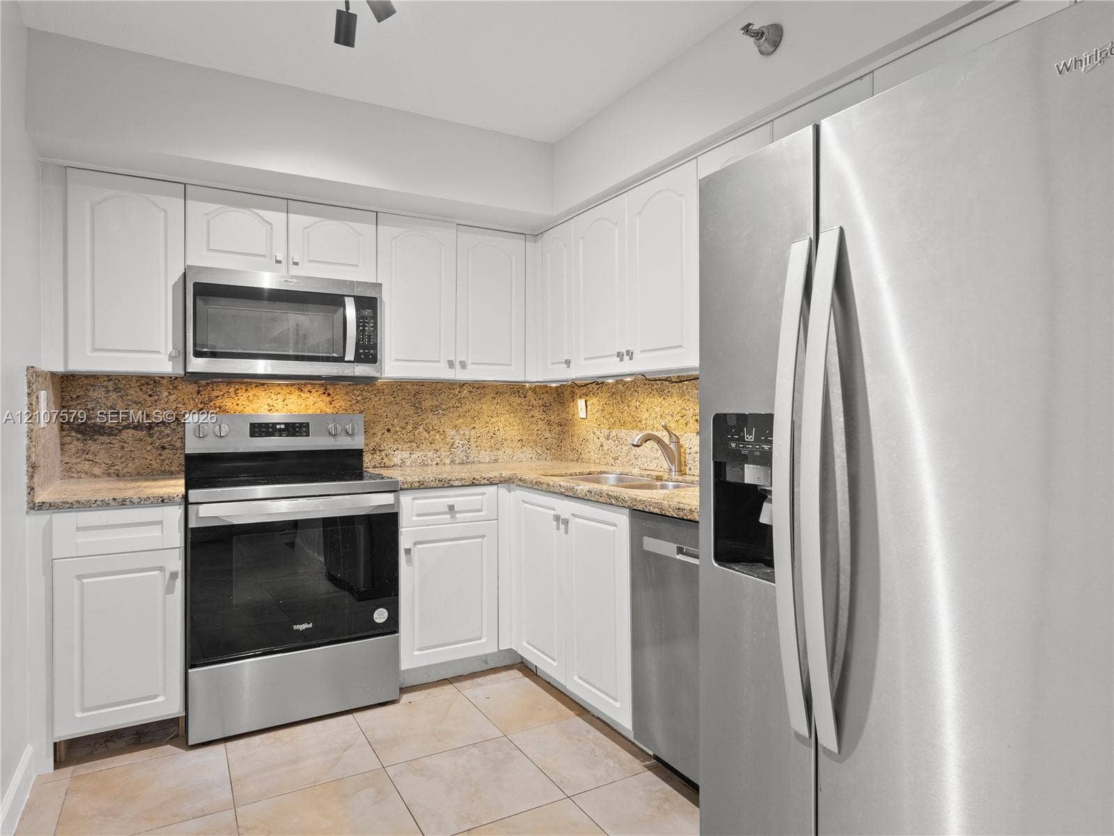 3300 NE 191st Street, #511, Aventura, FL 33180 Kitchen featuring white cabinetry, stone countertops, tiled flooring, and stainless steel appliances including a refrigerator, dishwasher, range, and built-in microwave