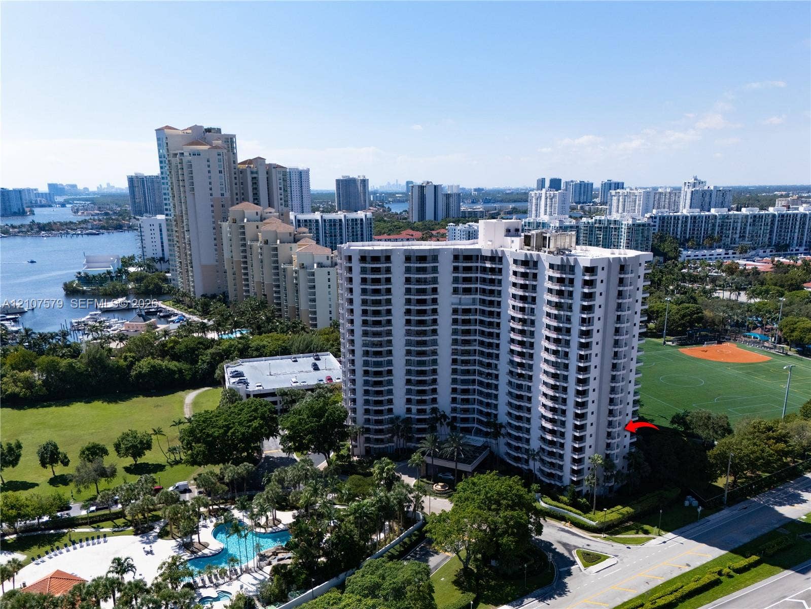 3300 NE 191st Street, #511, Aventura, FL 33180 High-rise residential building featuring expansive private balconies, swimming pool with deck, and proximity to adjacent recreational fields