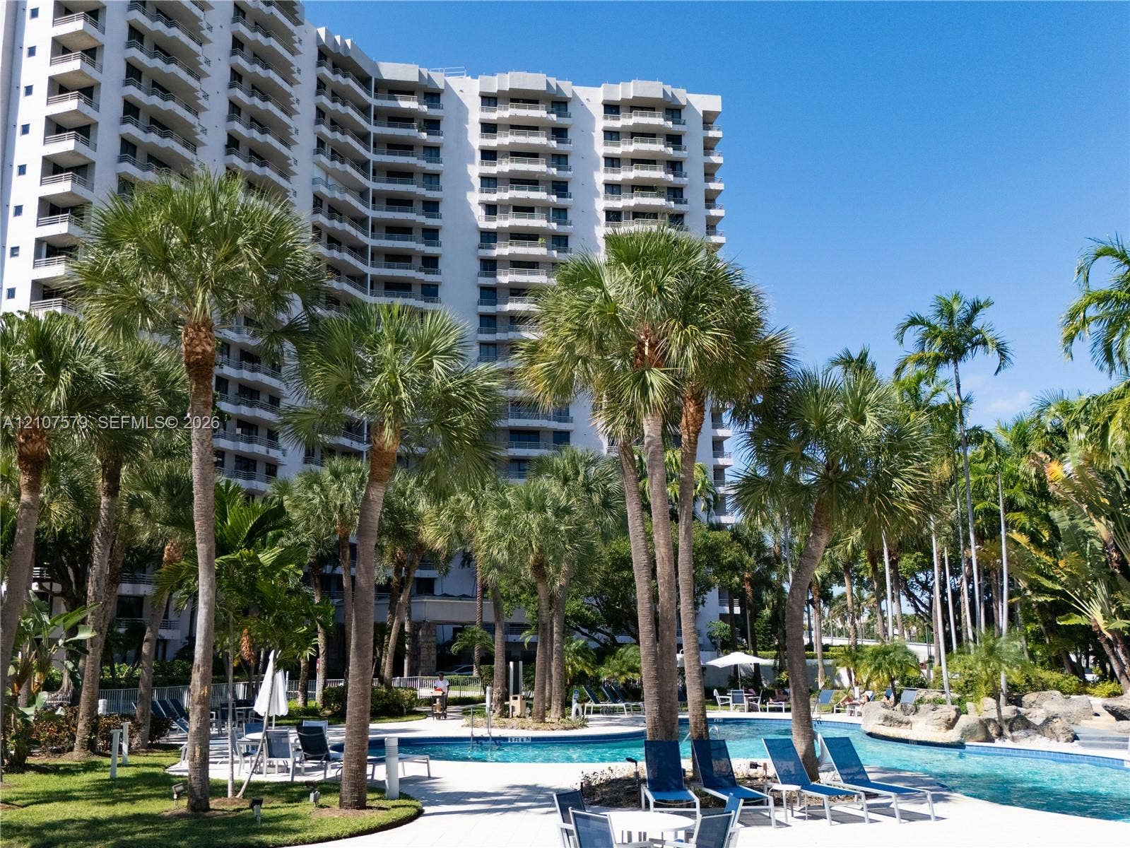 3300 NE 191st Street, #511, Aventura, FL 33180 Multi-story high-rise building featuring private balconies, expansive swimming pool, hardscaped pool deck, and mature tropical landscaping