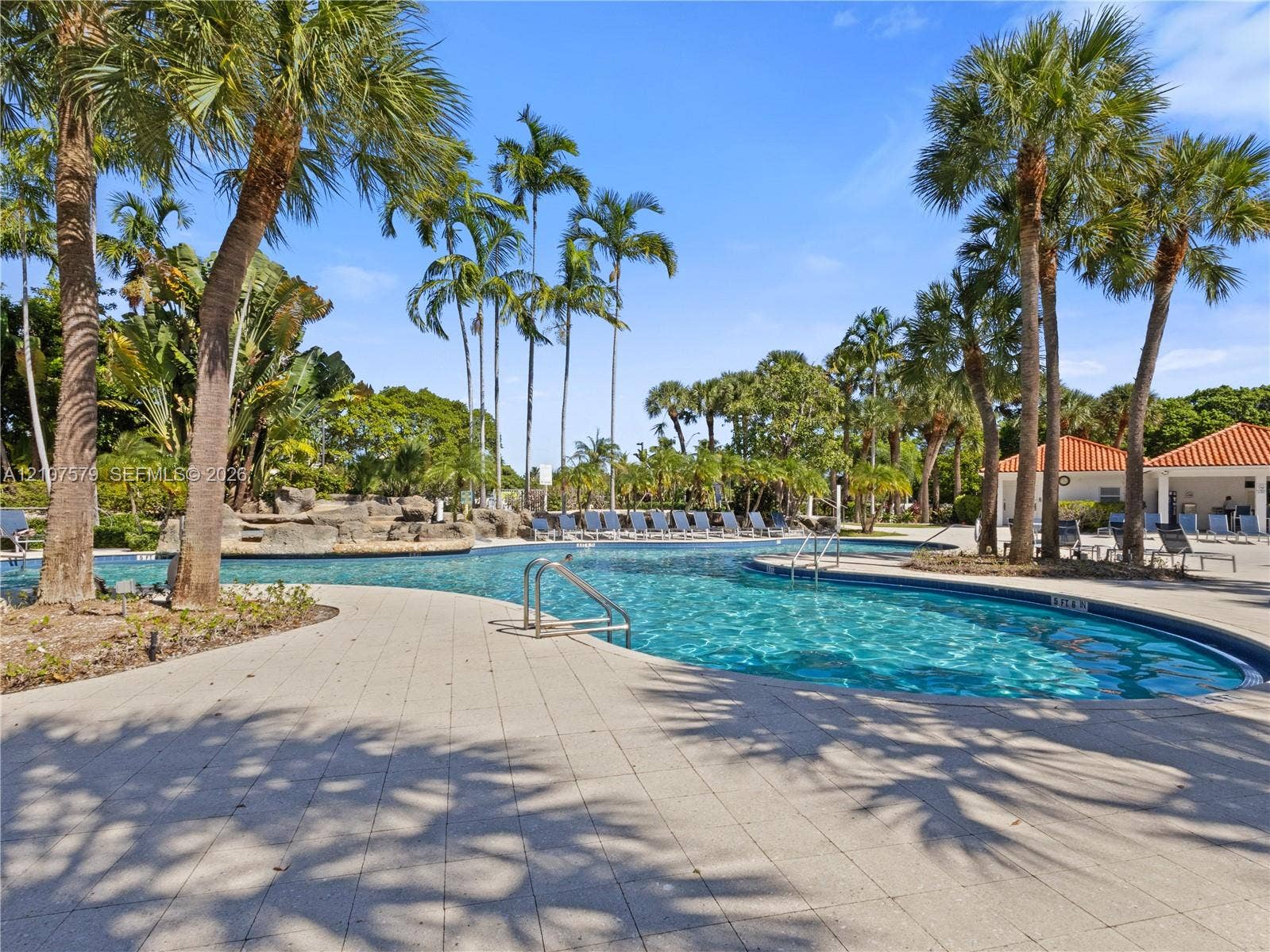 3300 NE 191st Street, #511, Aventura, FL 33180 Free-form swimming pool featuring rock-wall water features, expansive paver decking, and surrounding mature palm trees