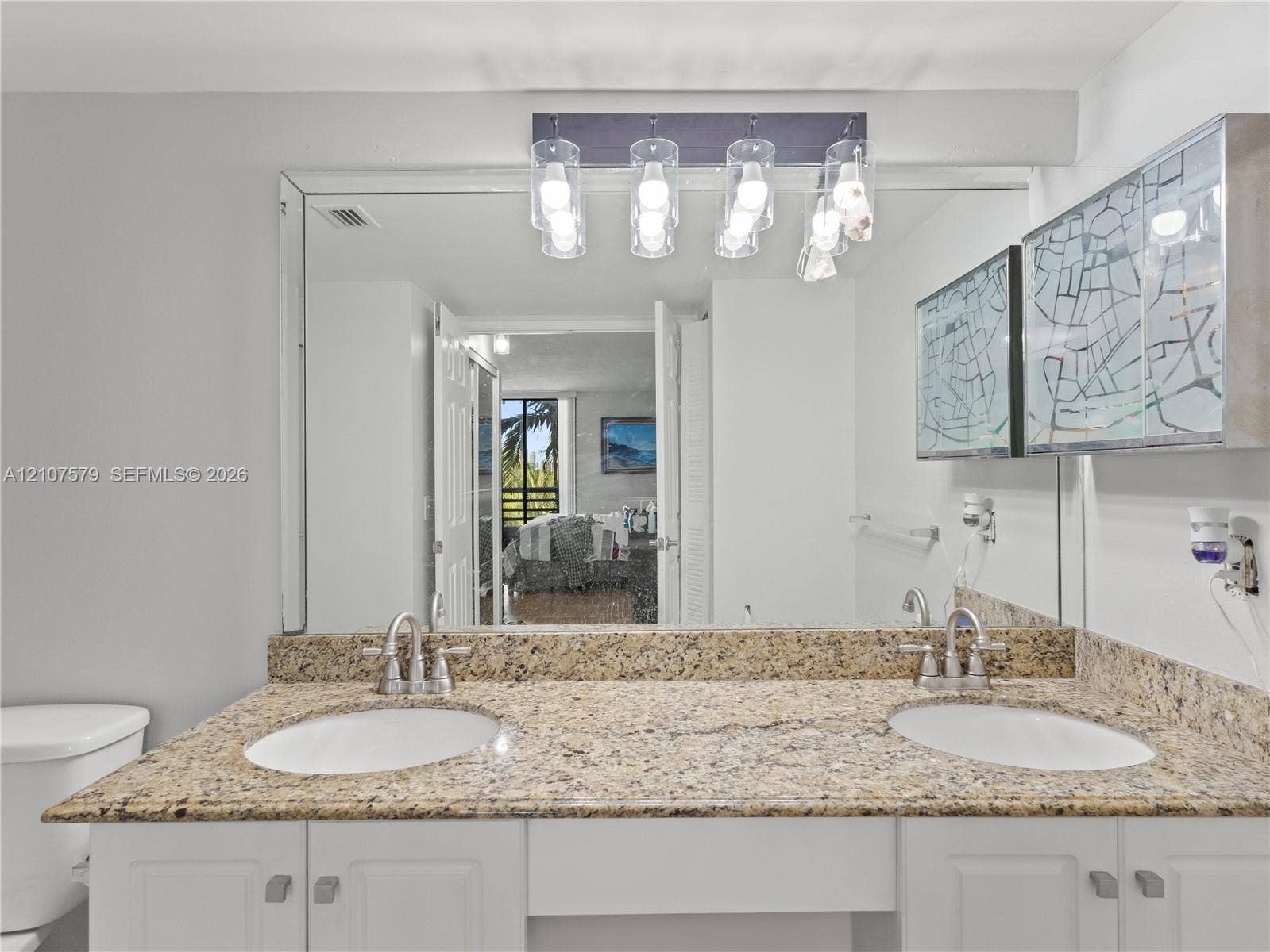 3300 NE 191st Street, #511, Aventura, FL 33180 Dual-sink vanity with stone countertop, white cabinetry, large wall-mounted mirror, and multi-bulb decorative light fixture