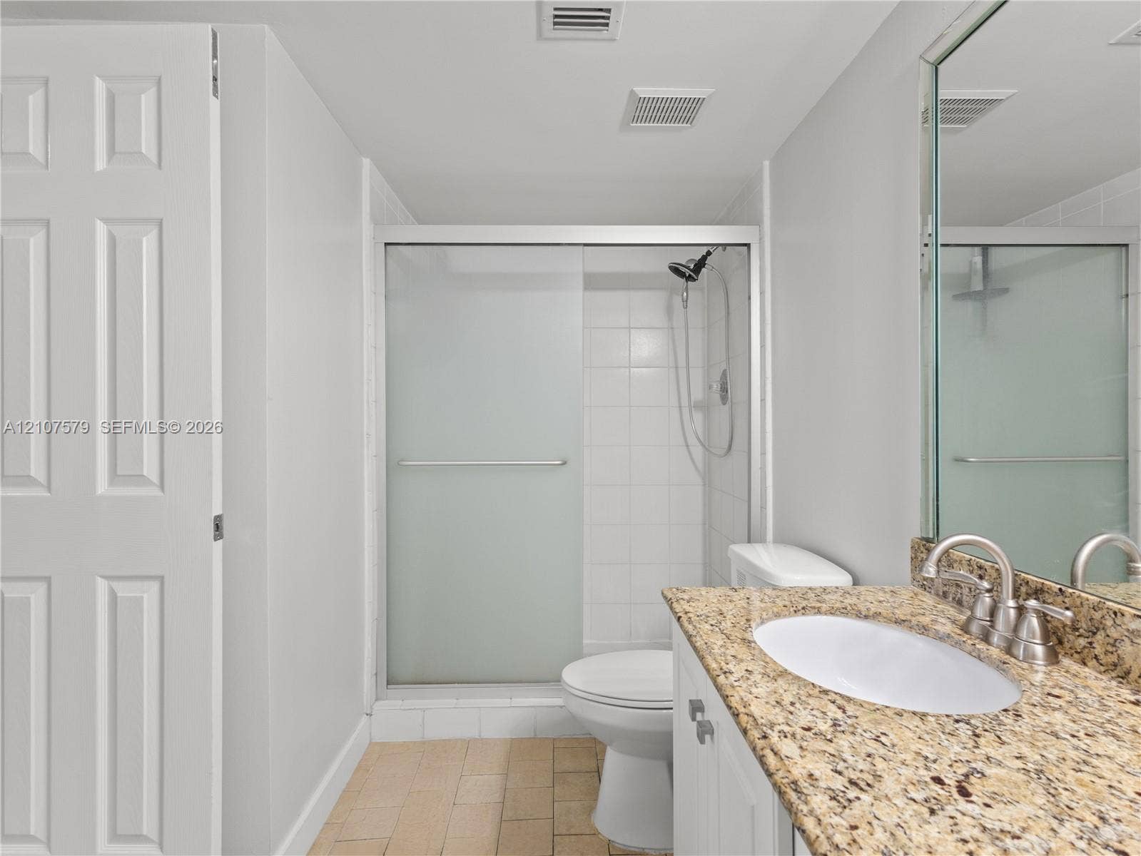 3300 NE 191st Street, #511, Aventura, FL 33180 Bathroom featuring stone-finish countertop with an undermount oval sink, sliding glass shower enclosure, white cabinetry, and tile flooring