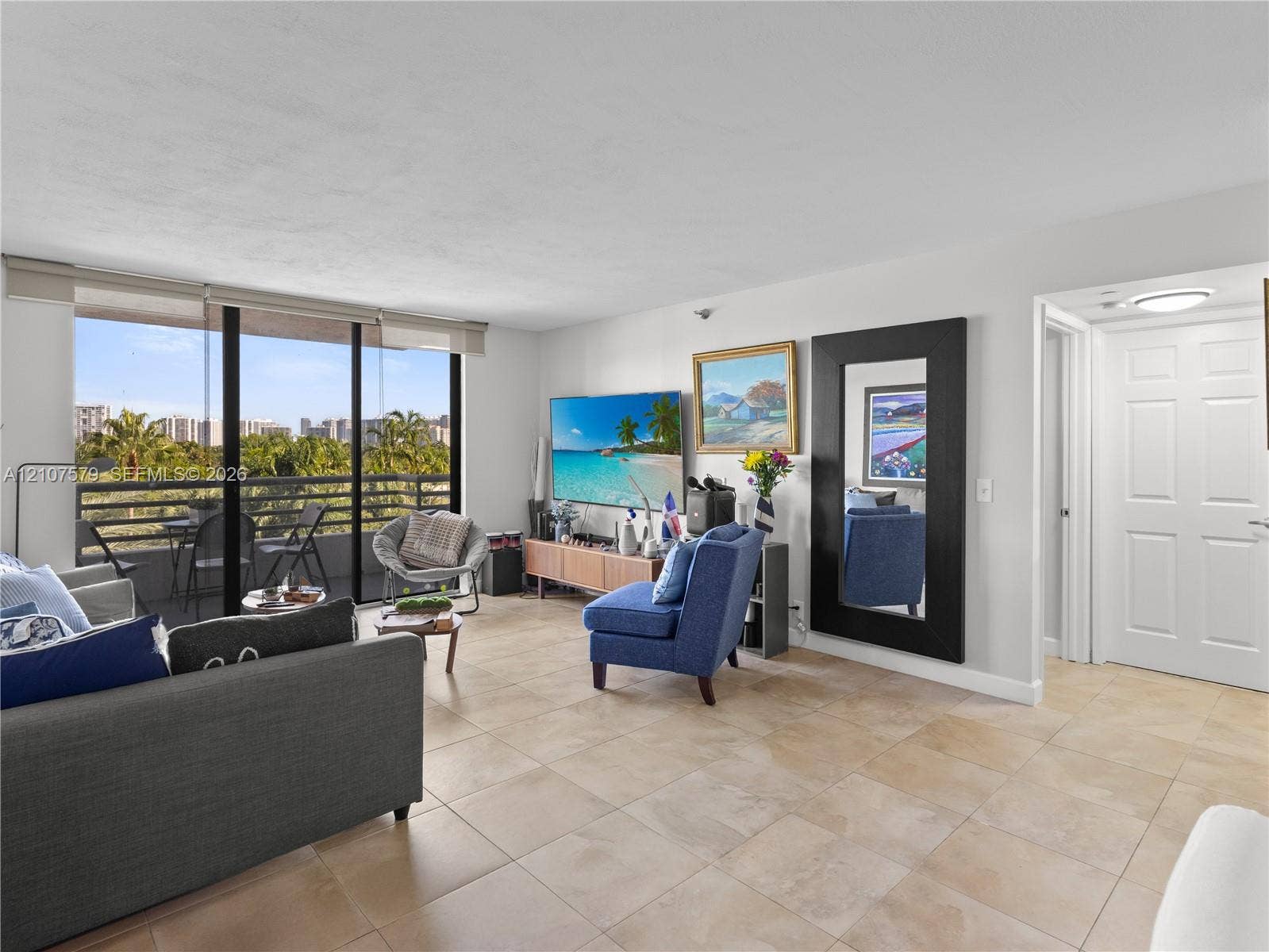 3300 NE 191st Street, #511, Aventura, FL 33180 Open-concept interior featuring large-format ceramic tile flooring, sliding glass door access to a covered balcony, and a multi-panel door