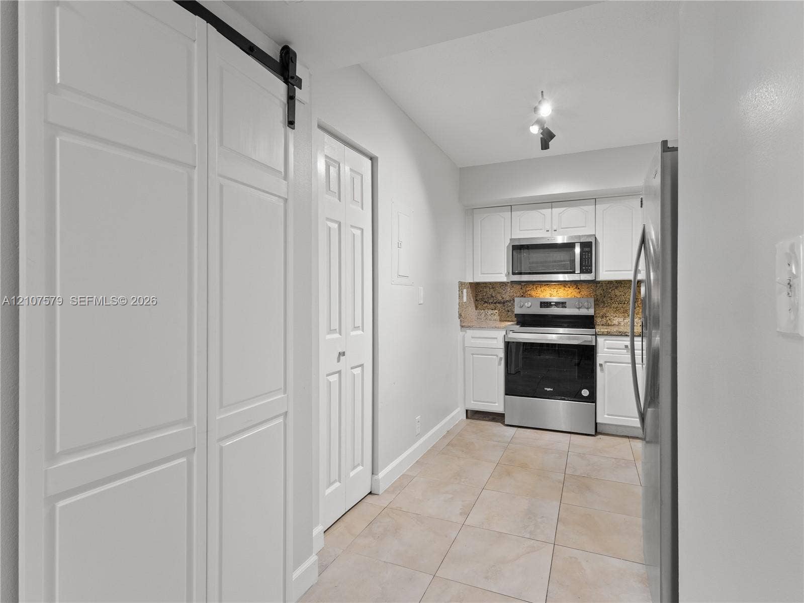 3300 NE 191st Street, #511, Aventura, FL 33180 Kitchen featuring white shaker-style cabinetry, stone-surface countertops, stainless steel appliances, tile flooring, and a white sliding barn door