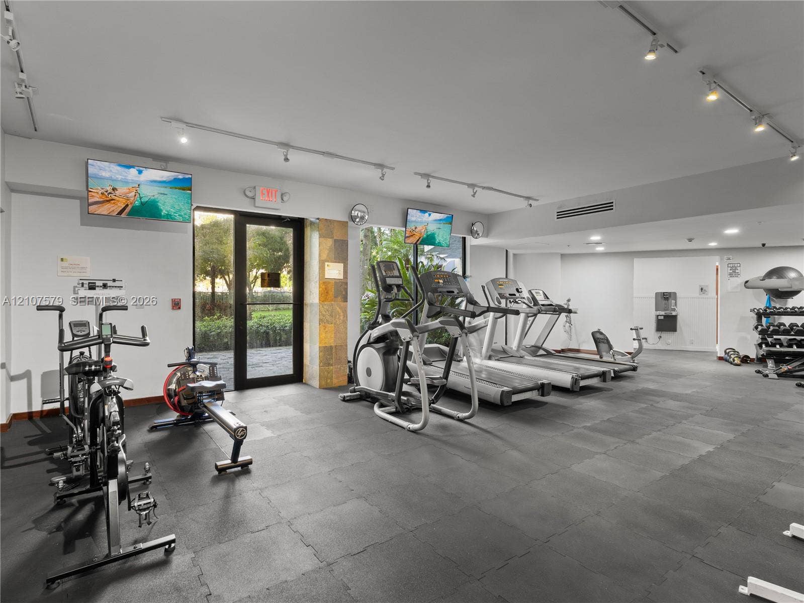 3300 NE 191st Street, #511, Aventura, FL 33180 Fitness facility featuring rubberized flooring, track lighting, a stone-accented pillar, and a glass-paneled exterior door