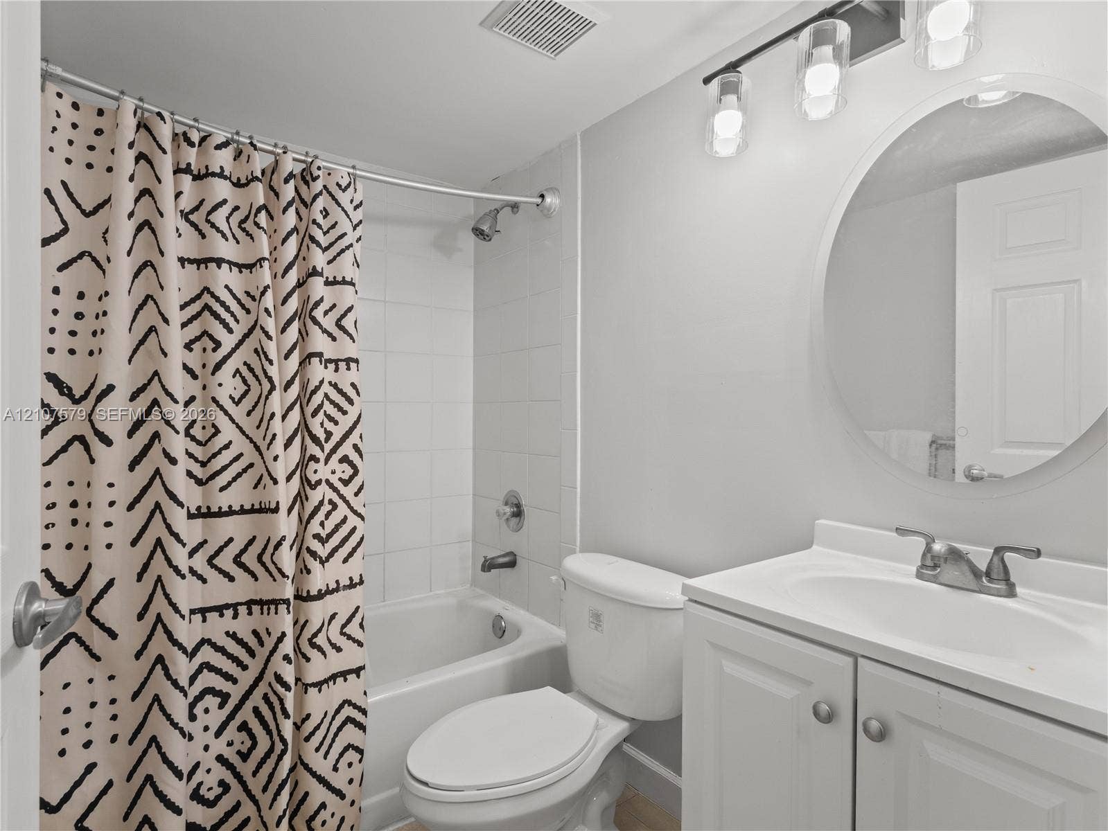 3300 NE 191st Street, #511, Aventura, FL 33180 Bathroom featuring a vanity with integrated sink, circular mirror, three-light fixture, and a white tile surround shower-tub combination
