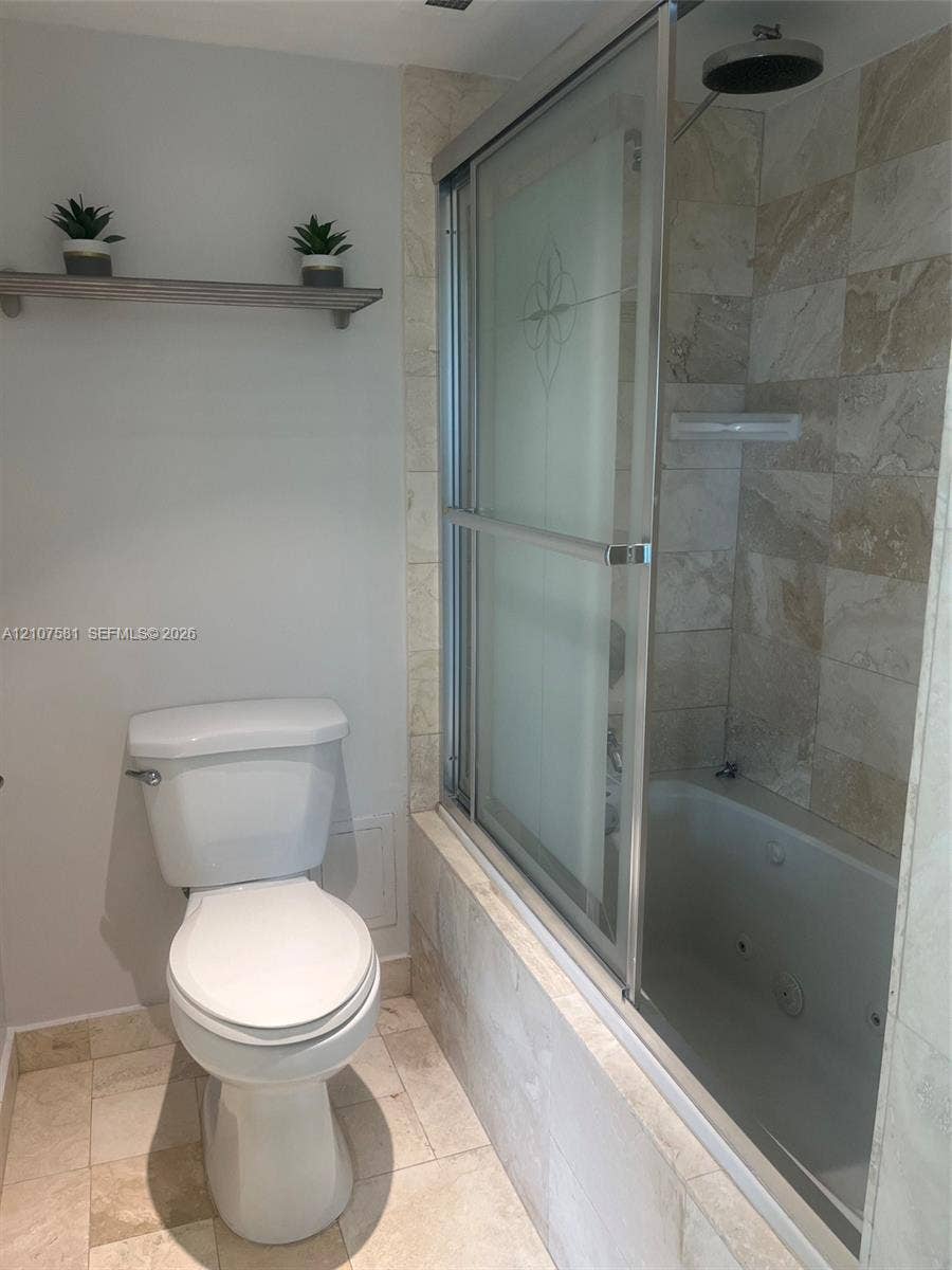 Tiled flooring with a built-in jetted tub, wall-mounted showerhead, and sliding glass shower enclosure