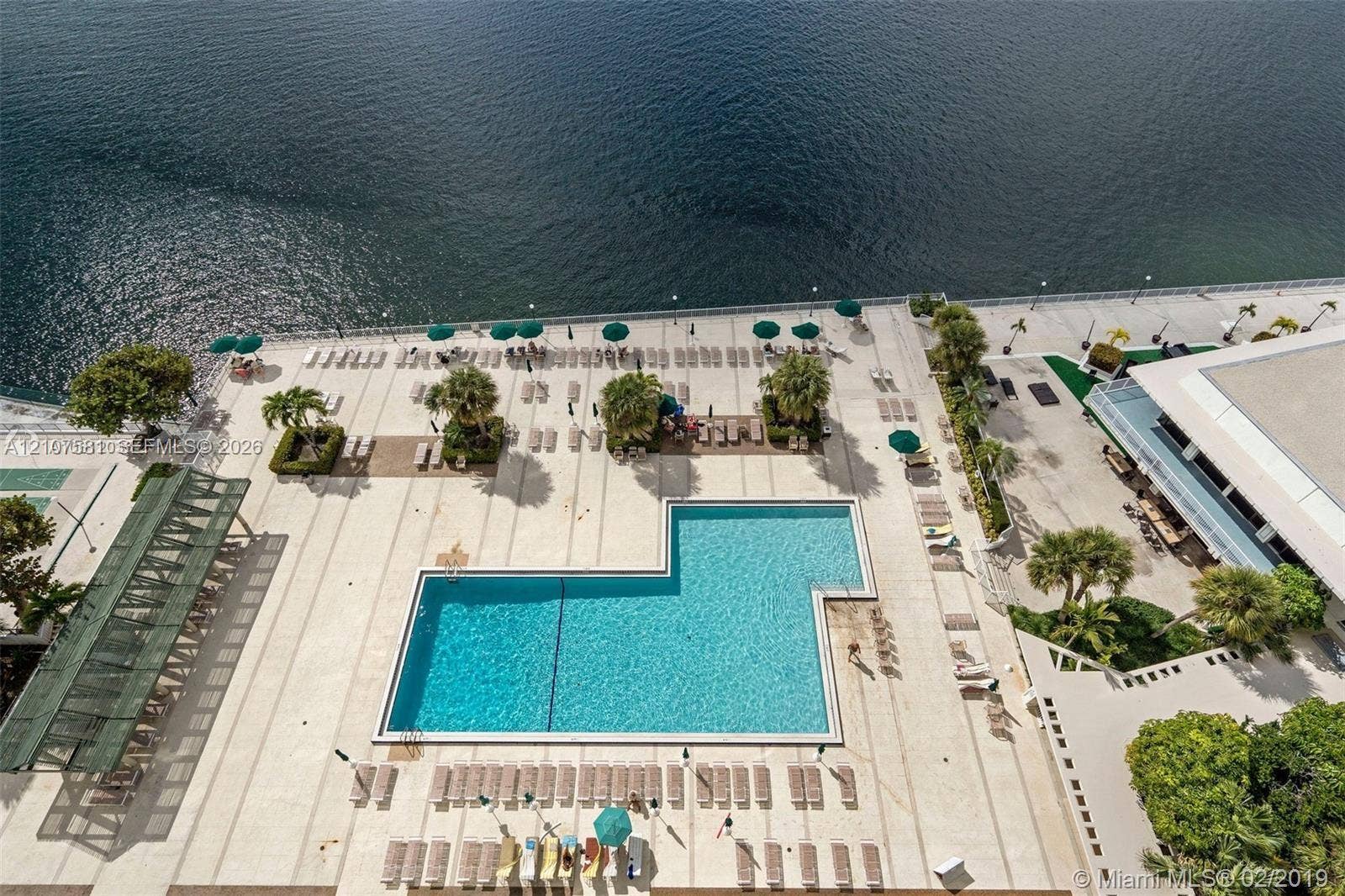 Expansive waterfront pool deck featuring a geometric swimming pool, extensive lounge seating, and mature landscaping