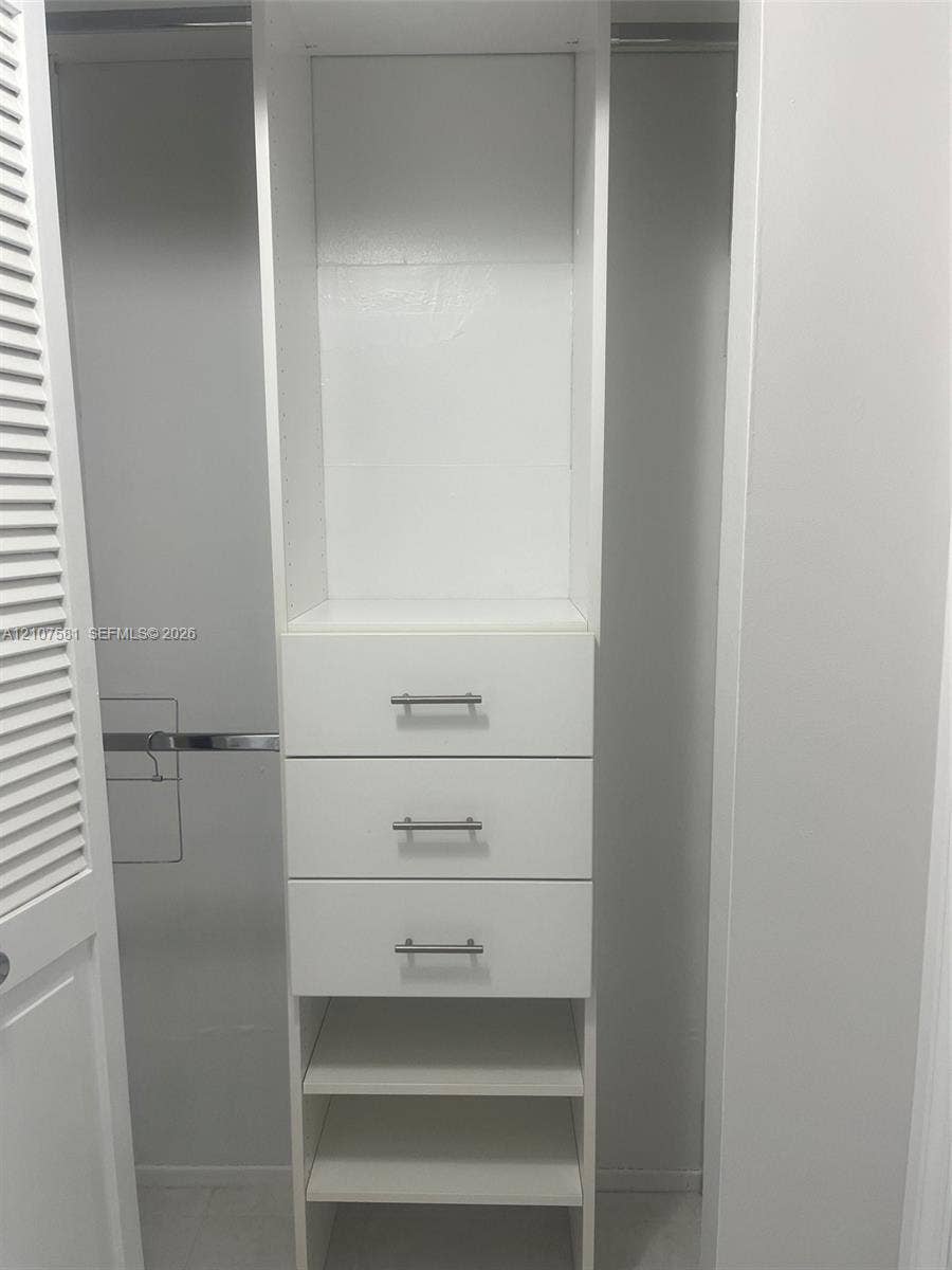 Built-in closet organization system featuring three drawers with brushed nickel pulls, multiple open shelves, and a clothes hanging rod