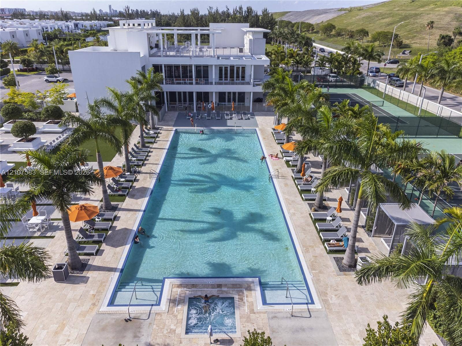 10270 NW 66th Street, #110, Doral, Doral, FL 33178 Rectangular swimming pool with integrated spa, stone-paver deck, professional-grade tennis court, and perimeter landscaping with palm trees
