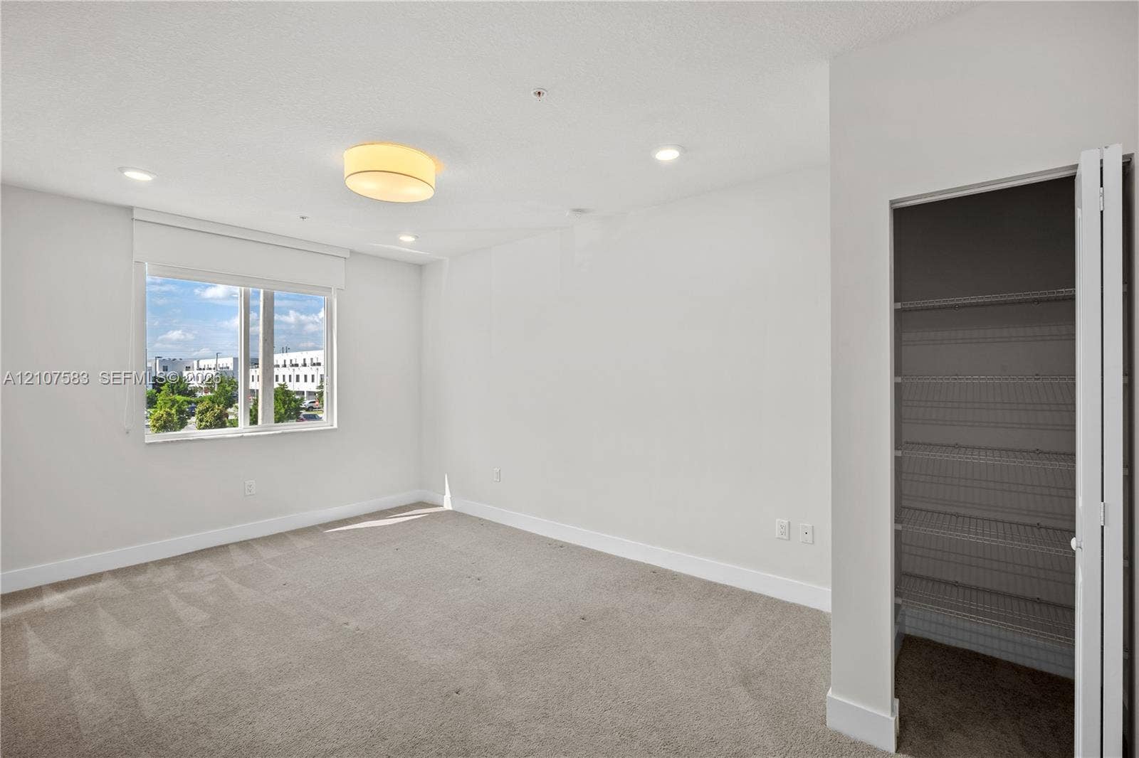10270 NW 66th Street, #110, Doral, Doral, FL 33178 Neutral-toned interior featuring wall-to-wall carpeting, recessed lighting, a central drum light fixture, large window with roller shade, and a closet with white bi-fold doors and built-in wire shelving