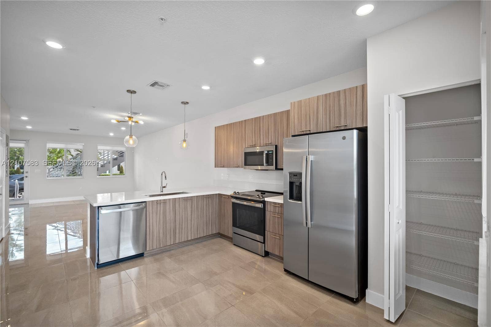 10270 NW 66th Street, #110, Doral, Doral, FL 33178 Kitchen featuring wood-finish cabinetry, stainless steel appliances, a peninsula with an integrated sink, polished tile flooring, and a walk-in pantry with built-in shelving