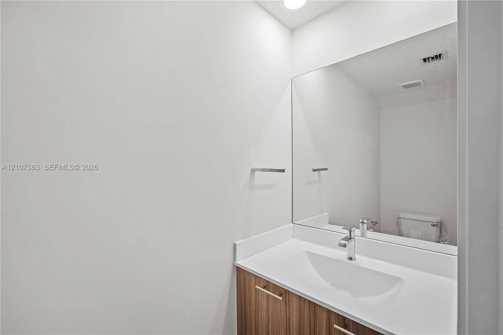 10270 NW 66th Street, #110, Doral, Doral, FL 33178 Vanity featuring a wood-finish cabinet, white solid-surface countertop with an integrated basin, wall-to-wall mirror, and a polished metal faucet