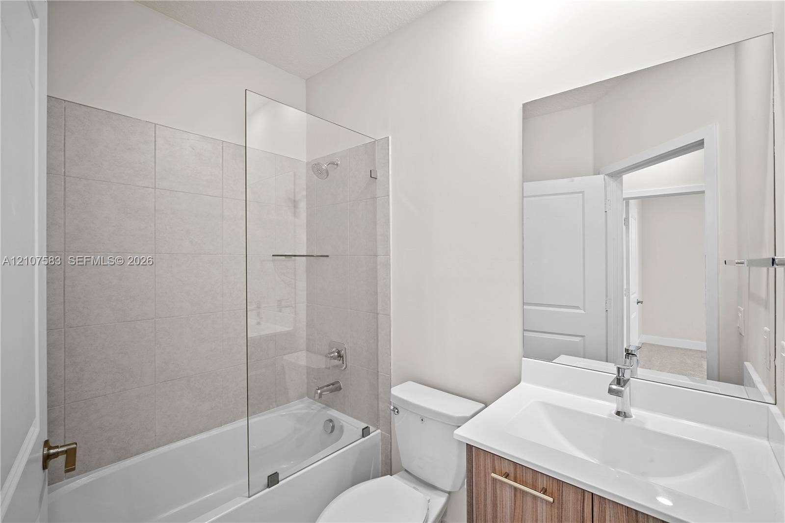 10270 NW 66th Street, #110, Doral, Doral, FL 33178 Bathroom featuring a tub-shower combination with floor-to-ceiling tile surround, a frameless glass panel, a wood-finish vanity with a rectangular integrated sink, and a large-format vanity mirror