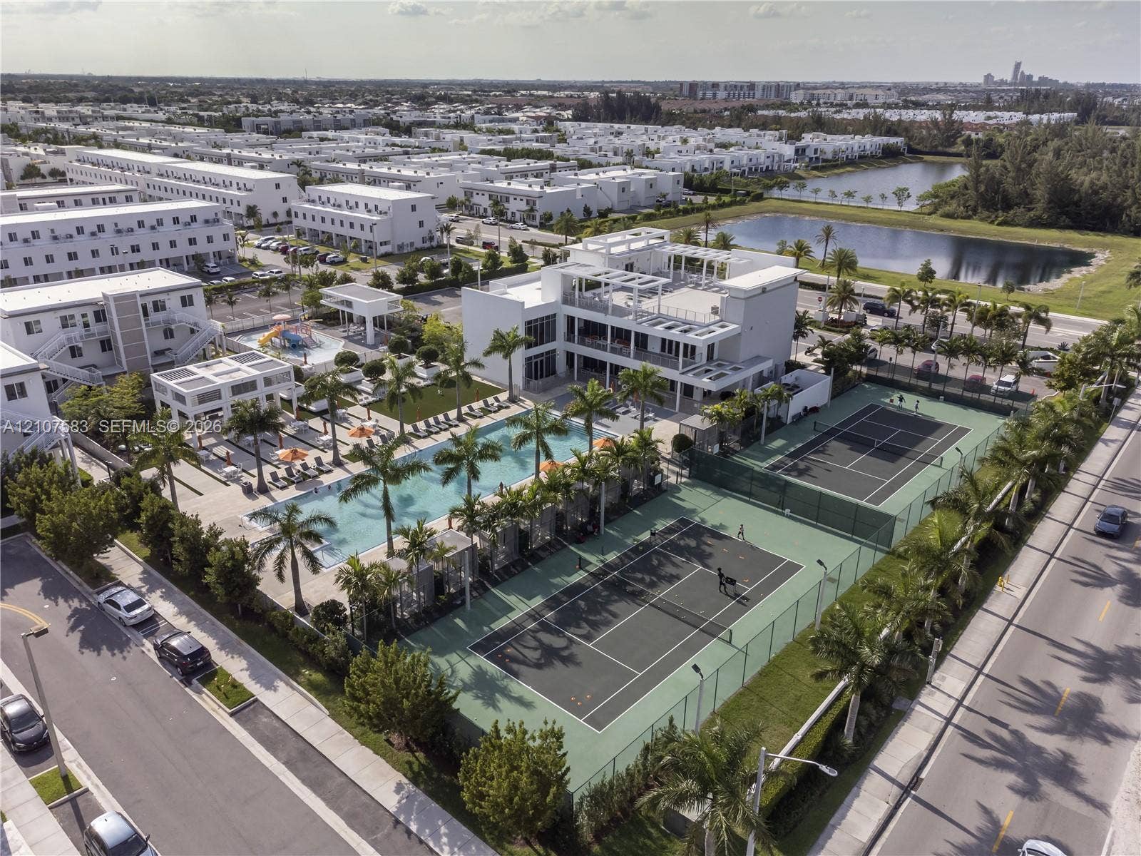 10270 NW 66th Street, #110, Doral, Doral, FL 33178 Aerial perspective of a community facility featuring a large swimming pool, two fenced tennis courts, and landscaped grounds with mature palm trees