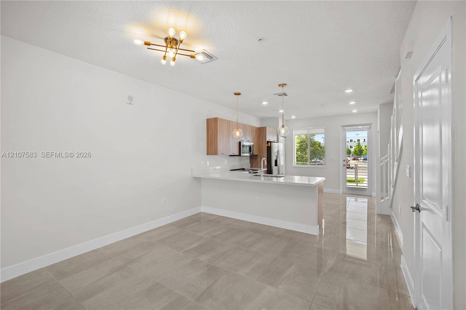 10270 NW 66th Street, #110, Doral, Doral, FL 33178 Open-concept interior featuring light-toned tile flooring, wood-finish cabinetry, a white countertop peninsula, and modern multi-light fixtures