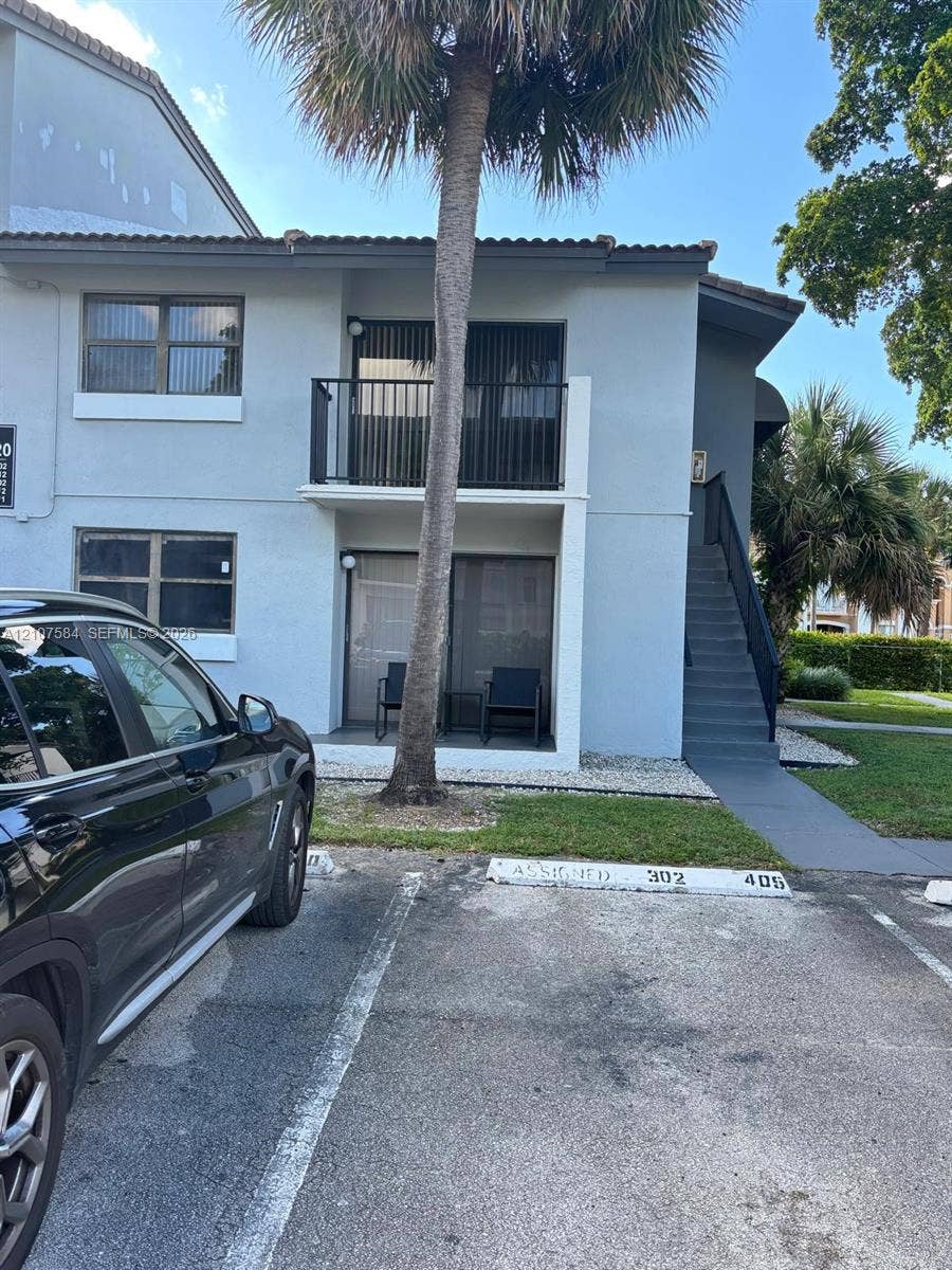 Two-story exterior featuring a private balcony, ground-level patio, exterior staircase, and assigned parking spaces