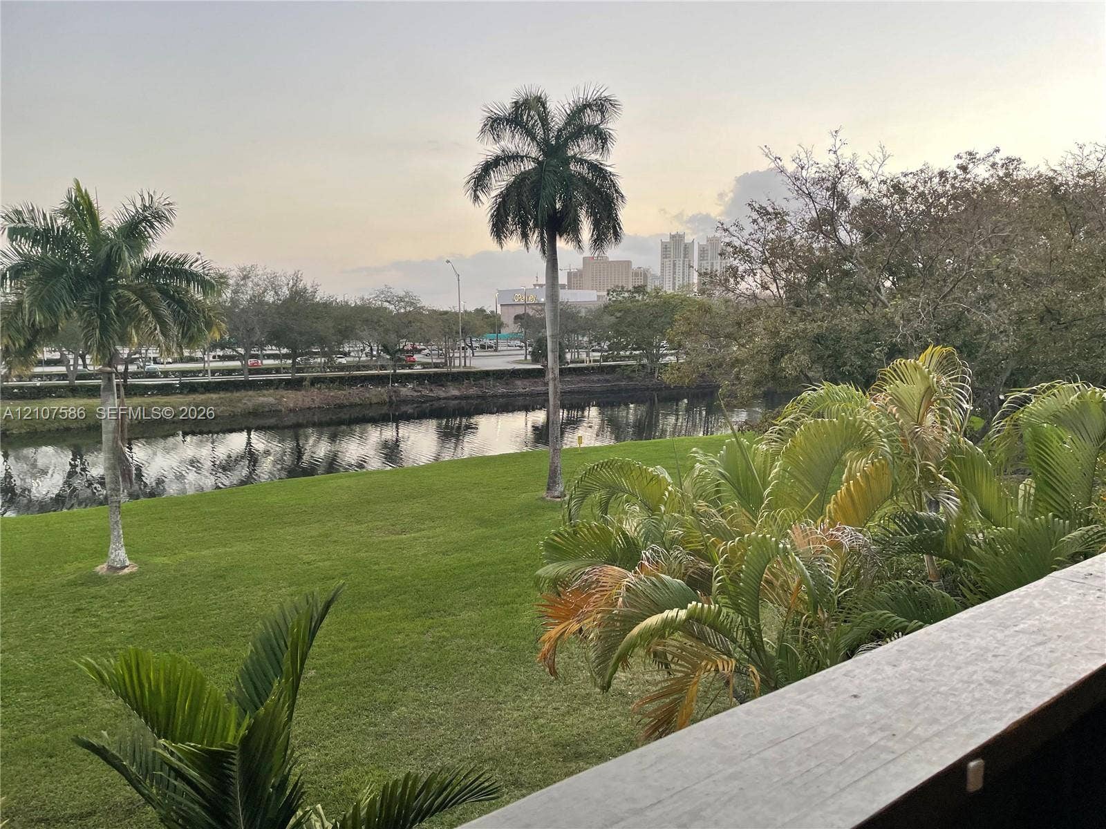 8335 SW 72nd Avenue, #306D, Miami, Miami, FL 33143 Outdoor balcony featuring a wood-finish railing overlooking a manicured lawn, a canal, and mature palm trees