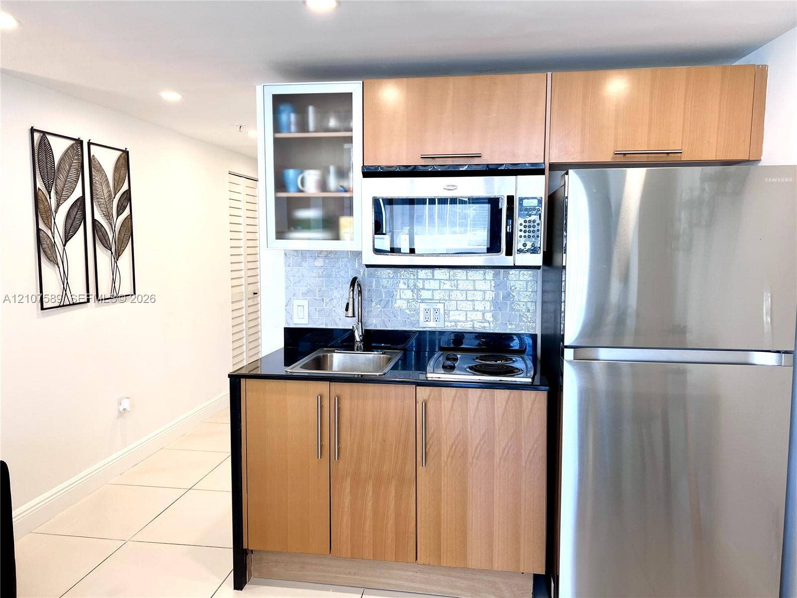 1750 N Bayshore Drive, #1218, Miami, Miami, FL 33132 Kitchenette featuring flat-panel wood-finish cabinetry, black stone countertops, a stainless steel refrigerator, built-in microwave, and a glass-front upper cabinet