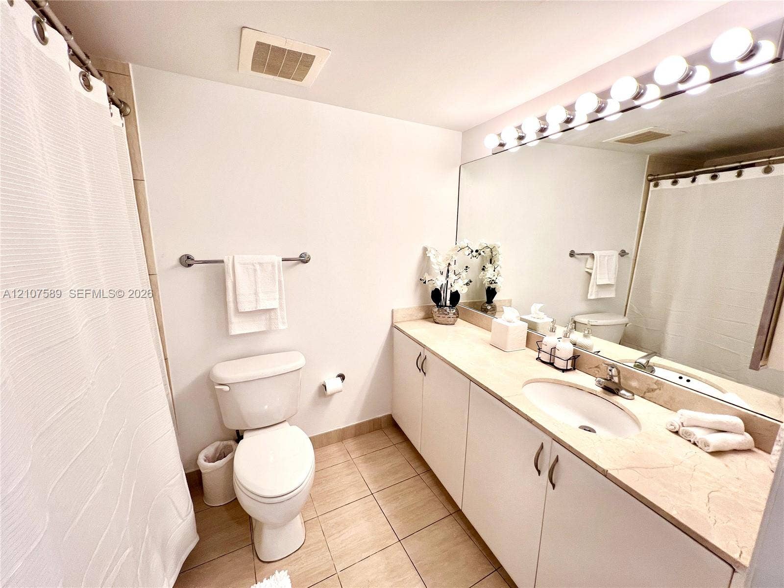1750 N Bayshore Drive, #1218, Miami, Miami, FL 33132 Bathroom featuring a full-width vanity with light-toned stone countertop, recessed oval sink, expansive wall-mounted mirror with integrated multi-bulb lighting, and tile flooring