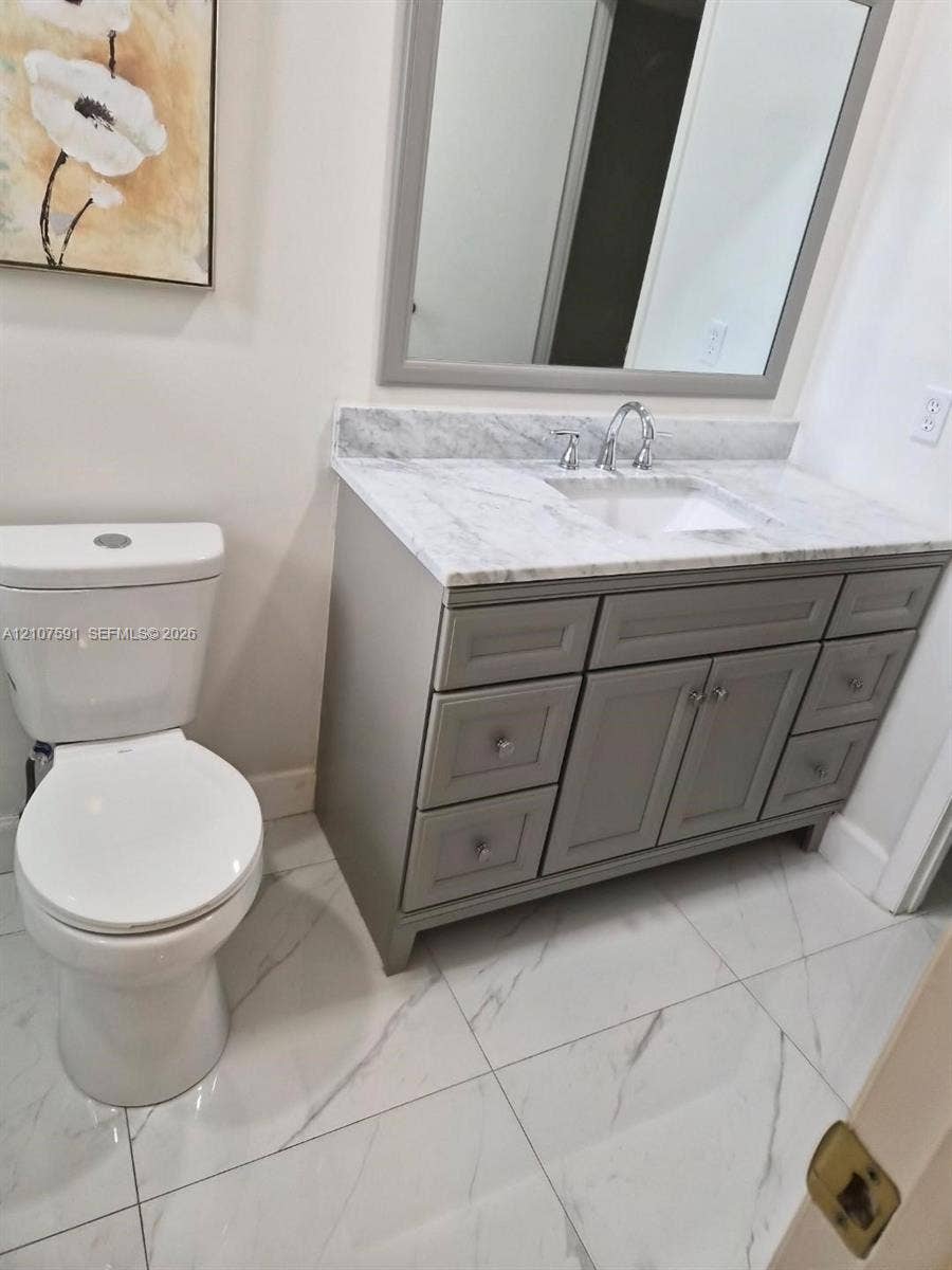 5003 NW 35th Street, #506, Lauderdale Lakes, FL 33319 Bathroom featuring a gray vanity with stone-top surfacing, undermount sink, framed mirror, and large-format tile flooring