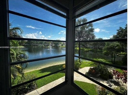 5003 NW 35th Street, #506, Lauderdale Lakes, FL 33319 Corner window enclosure featuring aluminum-framed horizontal jalousie windows, integrated blinds, and exterior water frontage with landscaped grounds