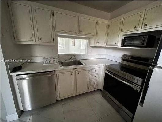 5003 NW 35th Street, #506, Lauderdale Lakes, FL 33319 Kitchen featuring white shaker-style cabinetry, stainless steel appliances, a drop-in stainless steel sink, solid surface countertops, and light-toned tile flooring