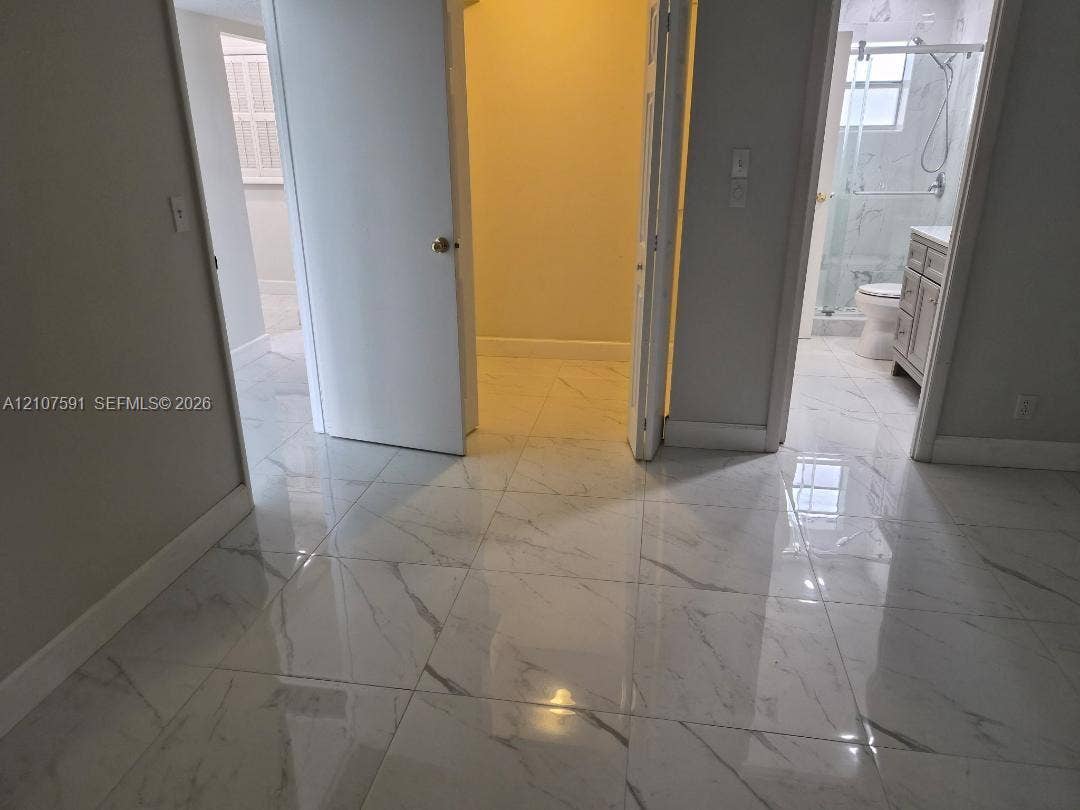 5003 NW 35th Street, #506, Lauderdale Lakes, FL 33319 Large-format porcelain tile flooring with veining, walk-in closet with interior lighting, and bathroom featuring a vanity with cabinet storage and a glass-enclosed shower