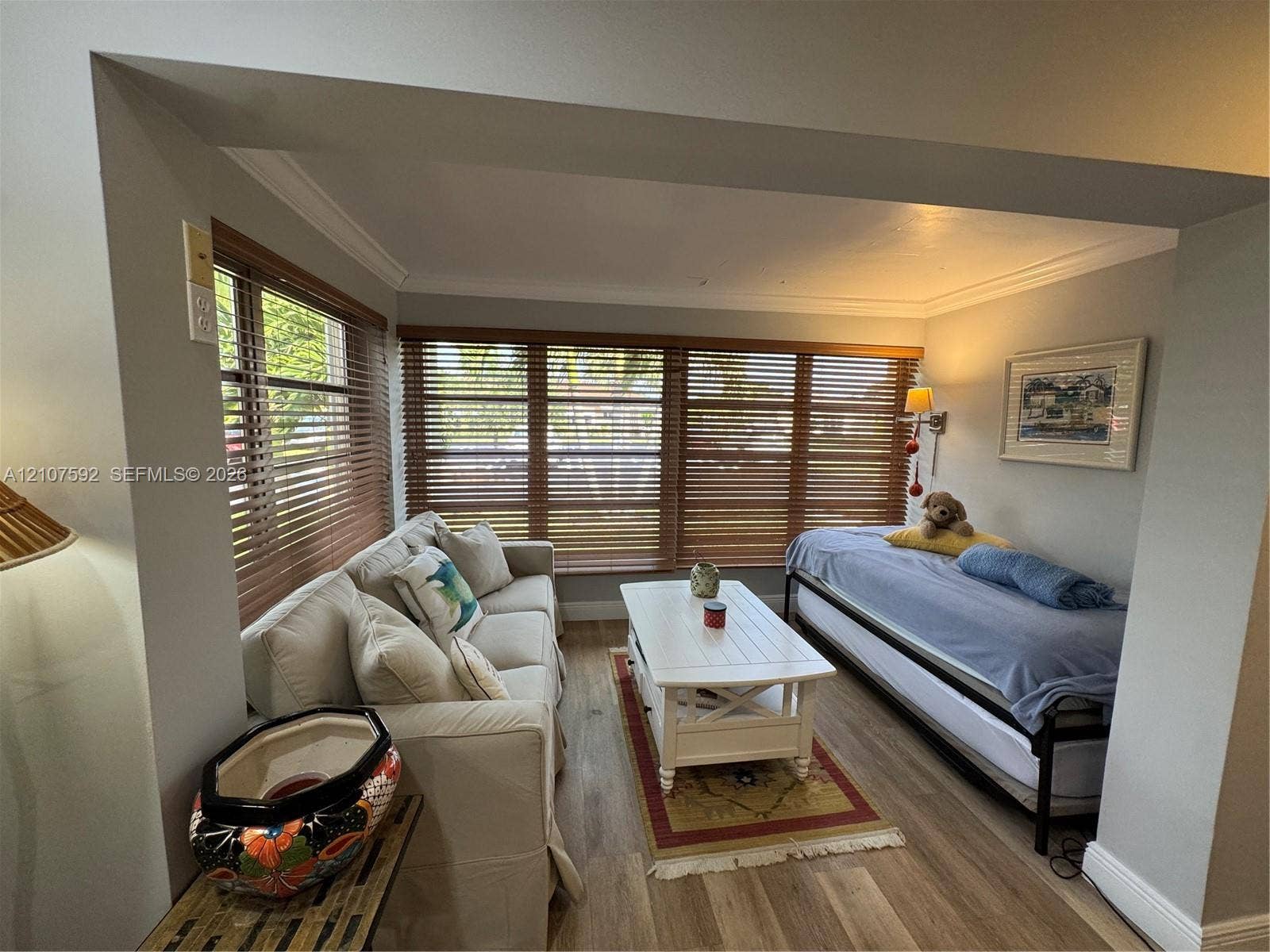 Room featuring wood-finish flooring, crown molding, and extensive natural light provided by multiple windows with horizontal slat blinds