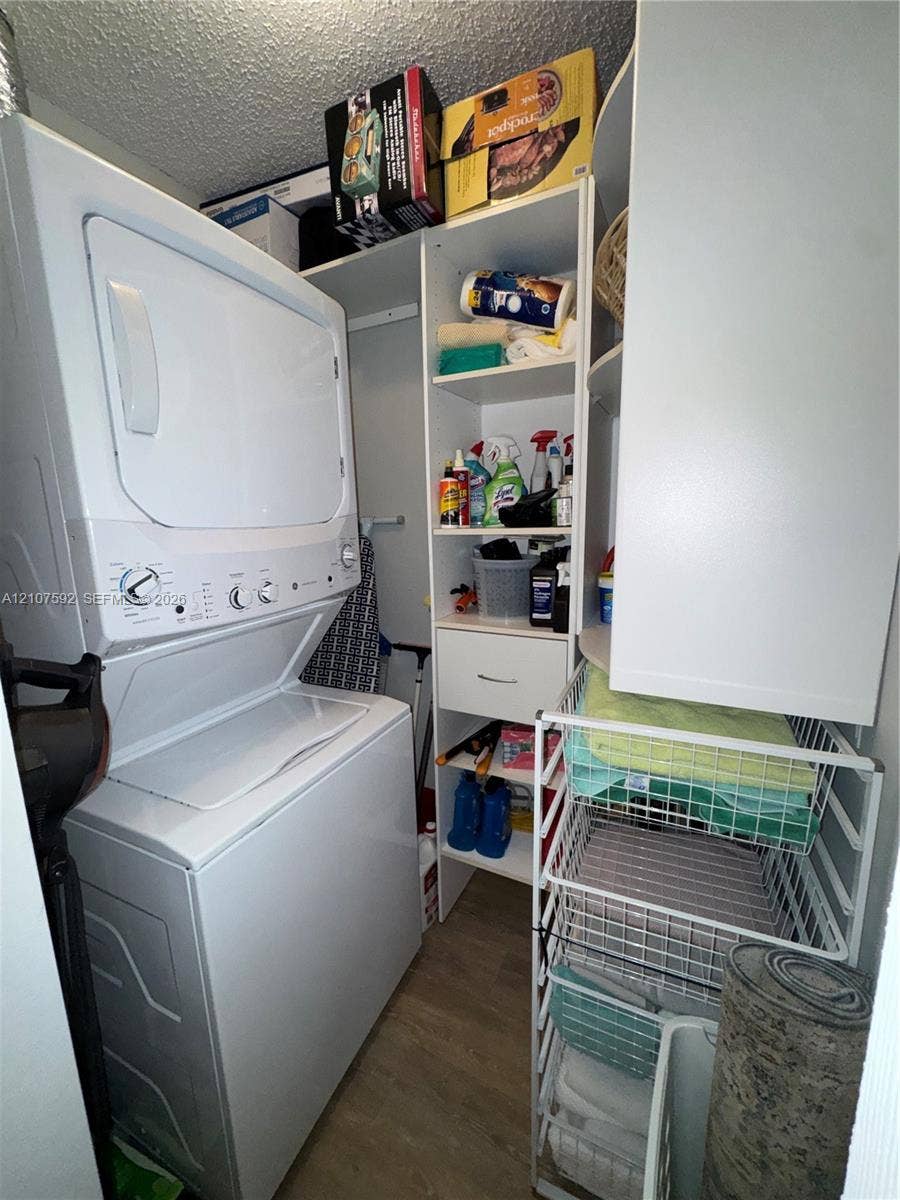 Laundry closet featuring a stackable washer and dryer, white built-in shelving unit, and wood-finish flooring