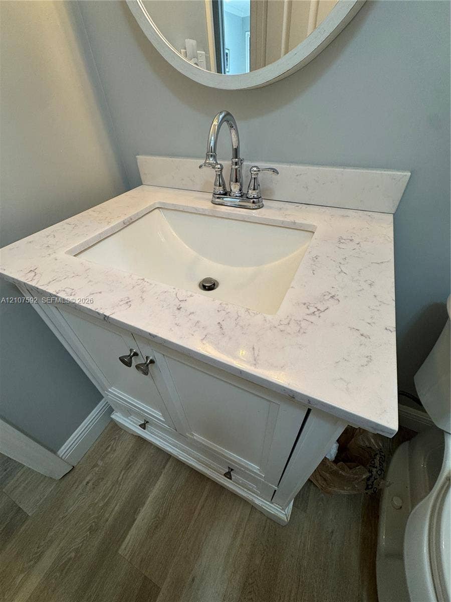 White vanity cabinet with integrated storage, engineered stone countertop, undermount sink, dual-handle chrome faucet, and circular wall-mounted mirror