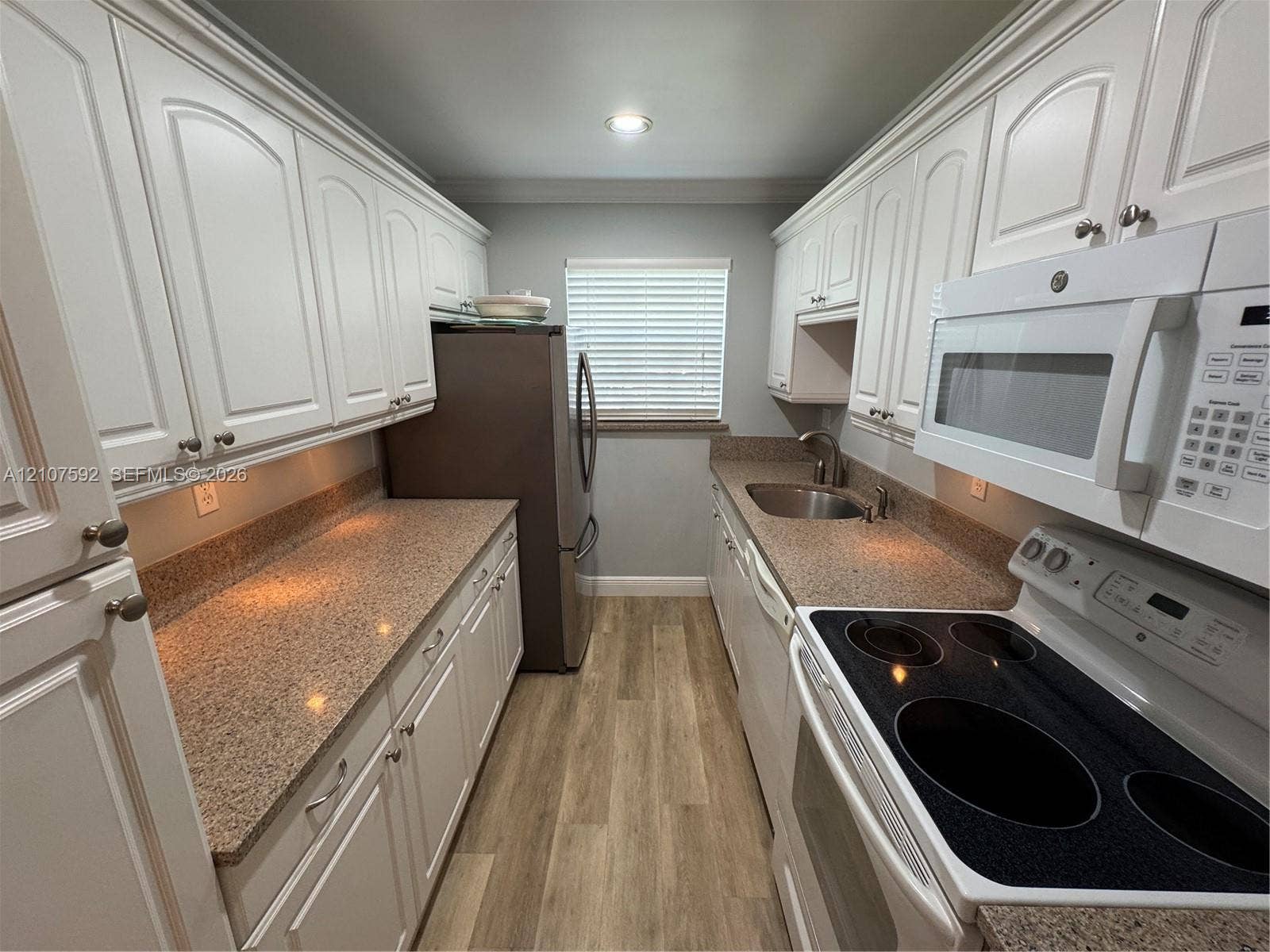 Galley kitchen featuring white raised-panel cabinetry, stone-patterned countertops, wood-finish flooring, and a stainless steel under-mount sink