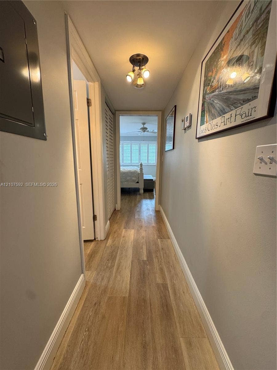 Hallway featuring wood-finish flooring, a multi-bulb flush-mount ceiling light fixture, and louvered closet doors