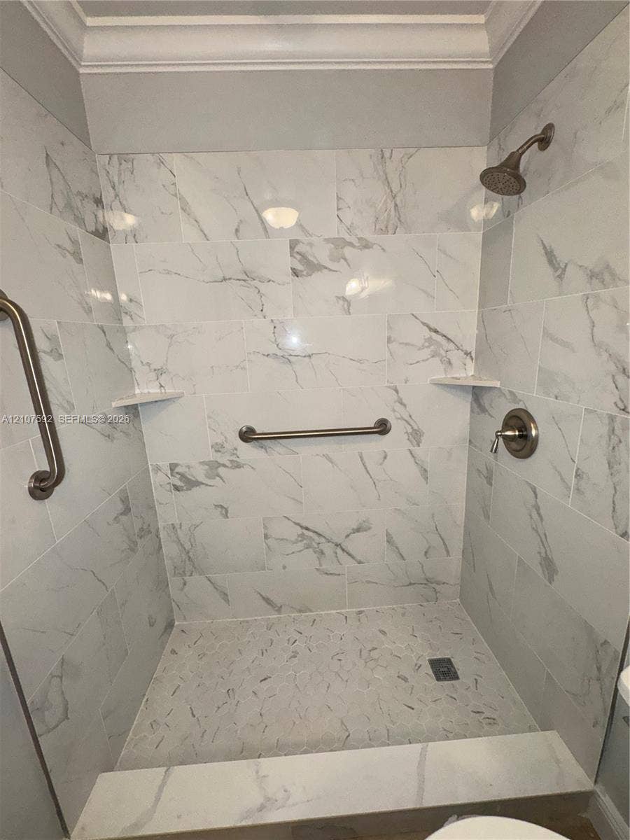 Walk-in shower featuring large-format stone-patterned wall tile, recessed corner shelving, a textured pebble floor, and brushed-finish plumbing fixtures