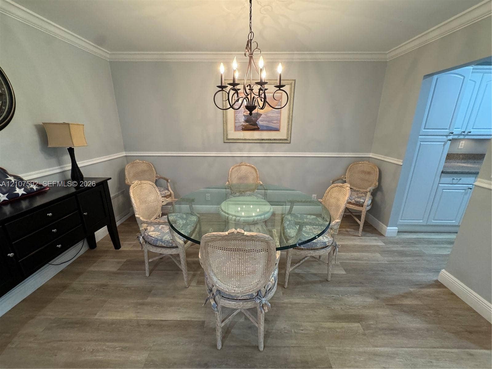 Dining area featuring wood-finish flooring, chair rail molding, crown molding, and a multi-arm candle-style chandelier