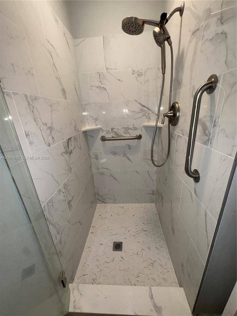 Walk-in shower featuring large-format stone-pattern wall tile, hexagonal floor tile, dual showerheads, and brushed-finish metal grab bars