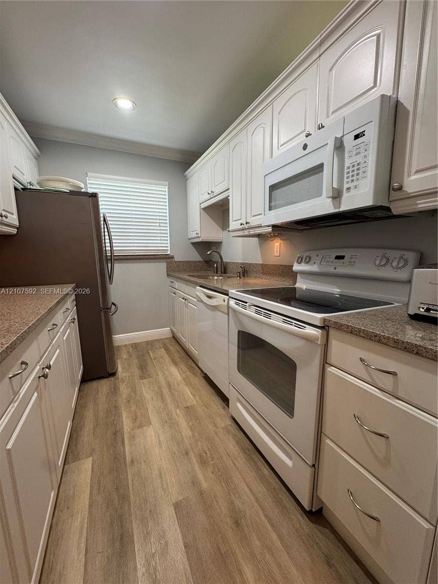 Kitchen featuring white cabinetry, wood-finish flooring, stone-surfaced countertops, a stainless steel sink, and recessed lighting