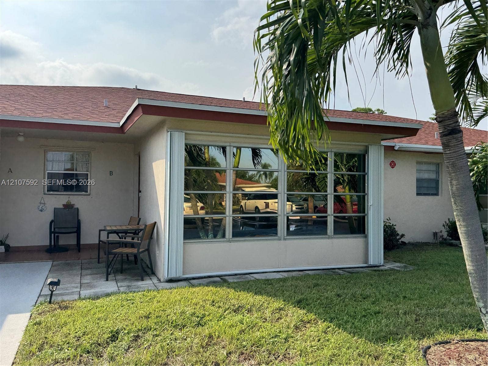 Stucco exterior featuring an enclosed sunroom with multi-pane windows, a concrete paver patio, and mature palm trees